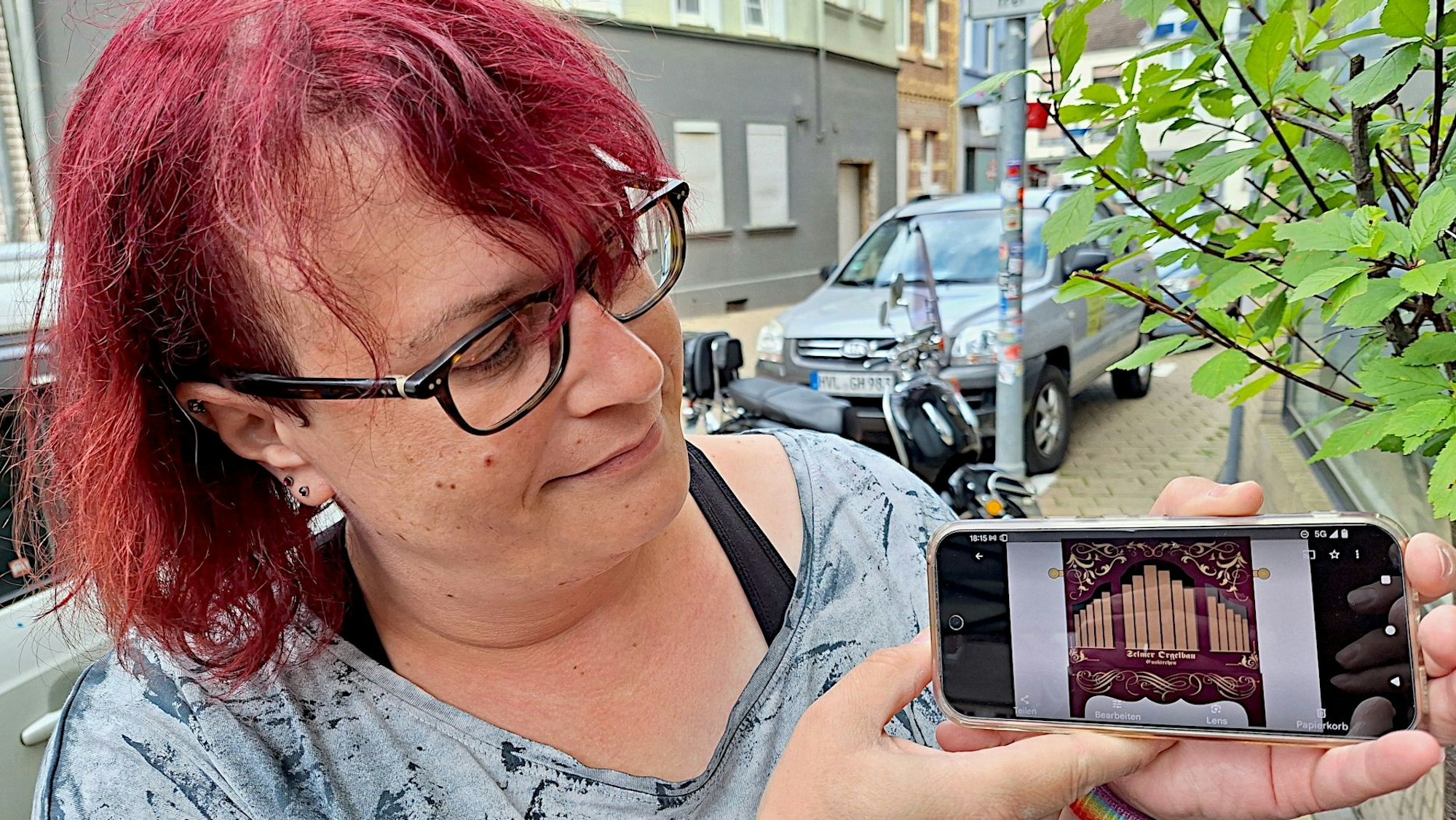Die Frau mit rot gefärbten Haaren zeigt auf ihrem Handy das Foto einer Drehorgel.