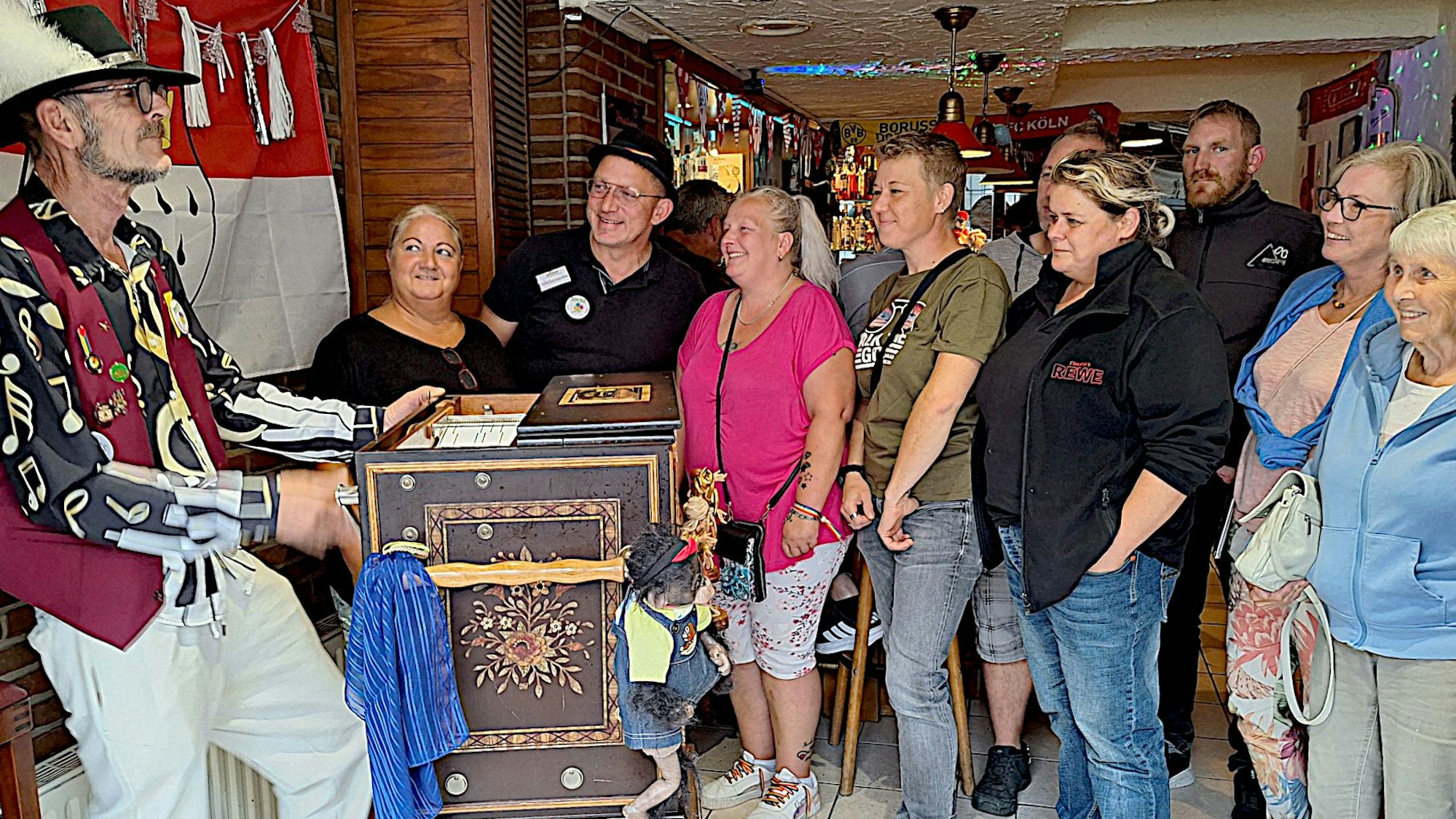 Neben dem Drehorgelspieler steht eine Gruppe von Menschen, die interessiert zusieht.