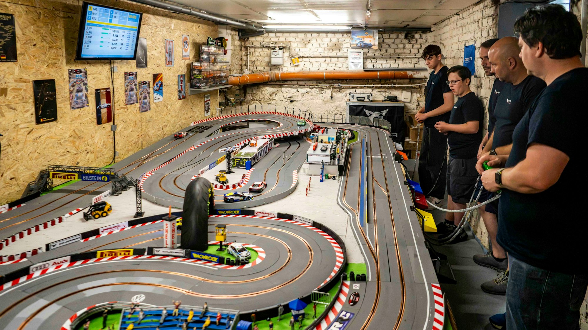 In einem Kellerraum befindet sich eine große Carrera-Rennbahn, daneben stehen mehrere Spieler mit ihren Controllern.