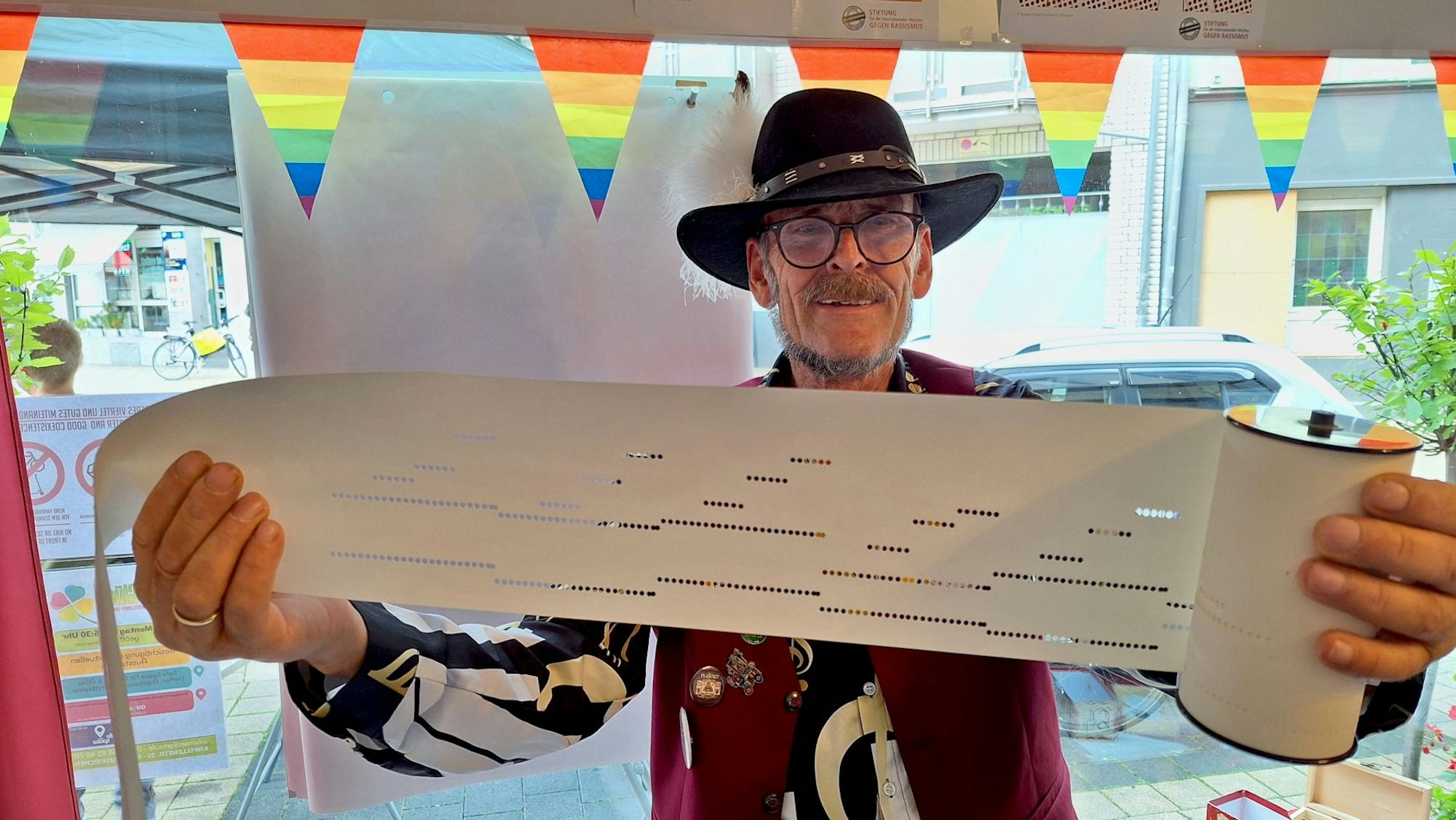 Der Drehorgelspieler, der einen schwarzen Hut trägt, zeigt die Lochrolle einer Drehorgel.