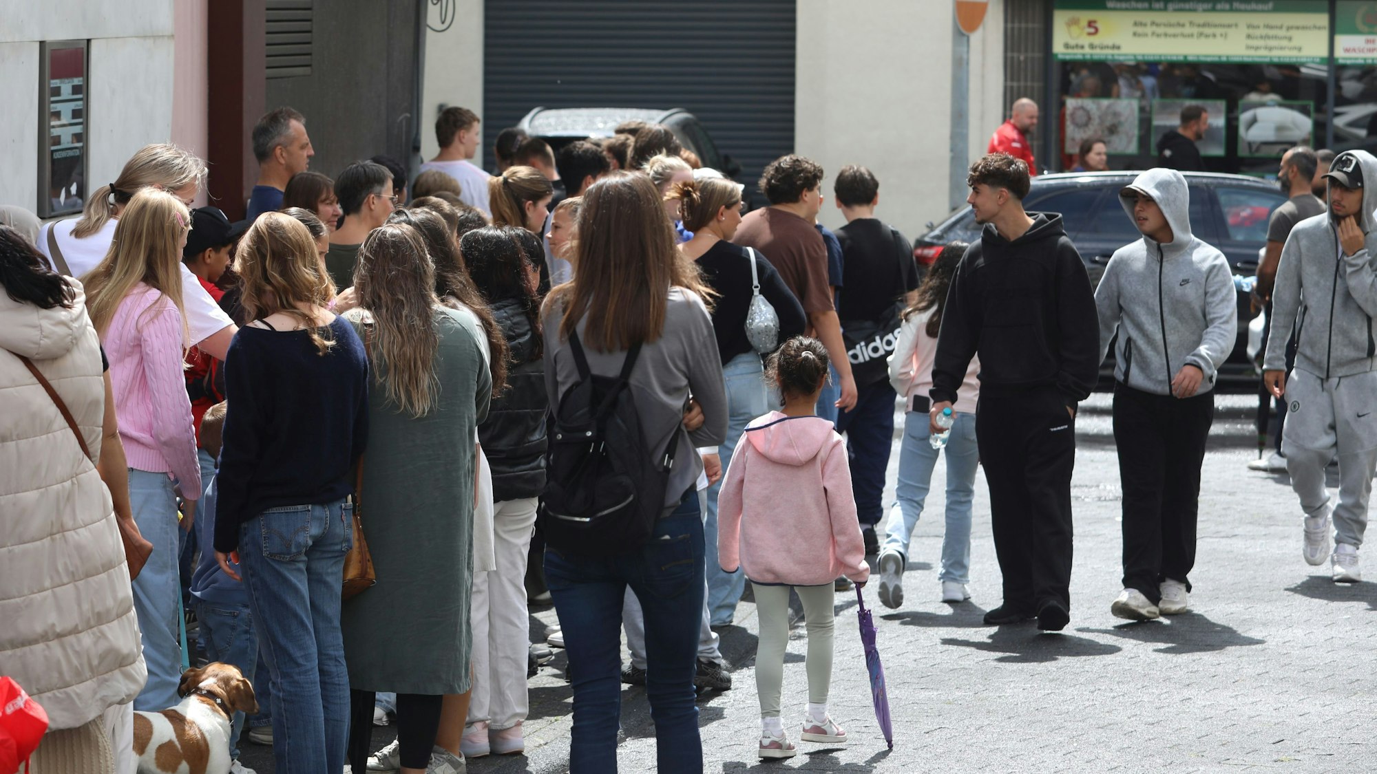 Menschen stehen in einer langen Schlange auf einem Gehweg und der Straße.