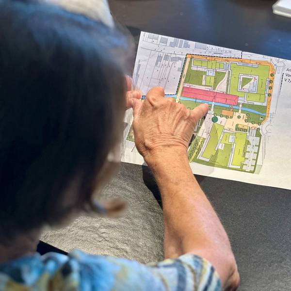 Eine Frau beugt sich über einen Plan und zeigt mit dem Finger auf etwas auf dem Plan.