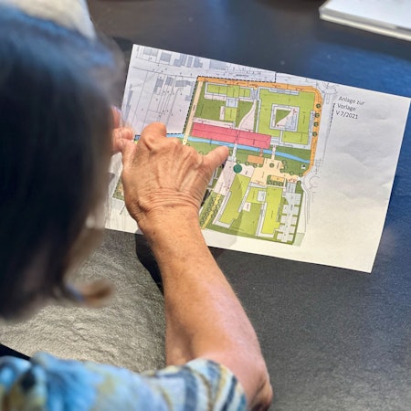 Eine Frau beugt sich über einen Plan und zeigt mit dem Finger auf etwas auf dem Plan.