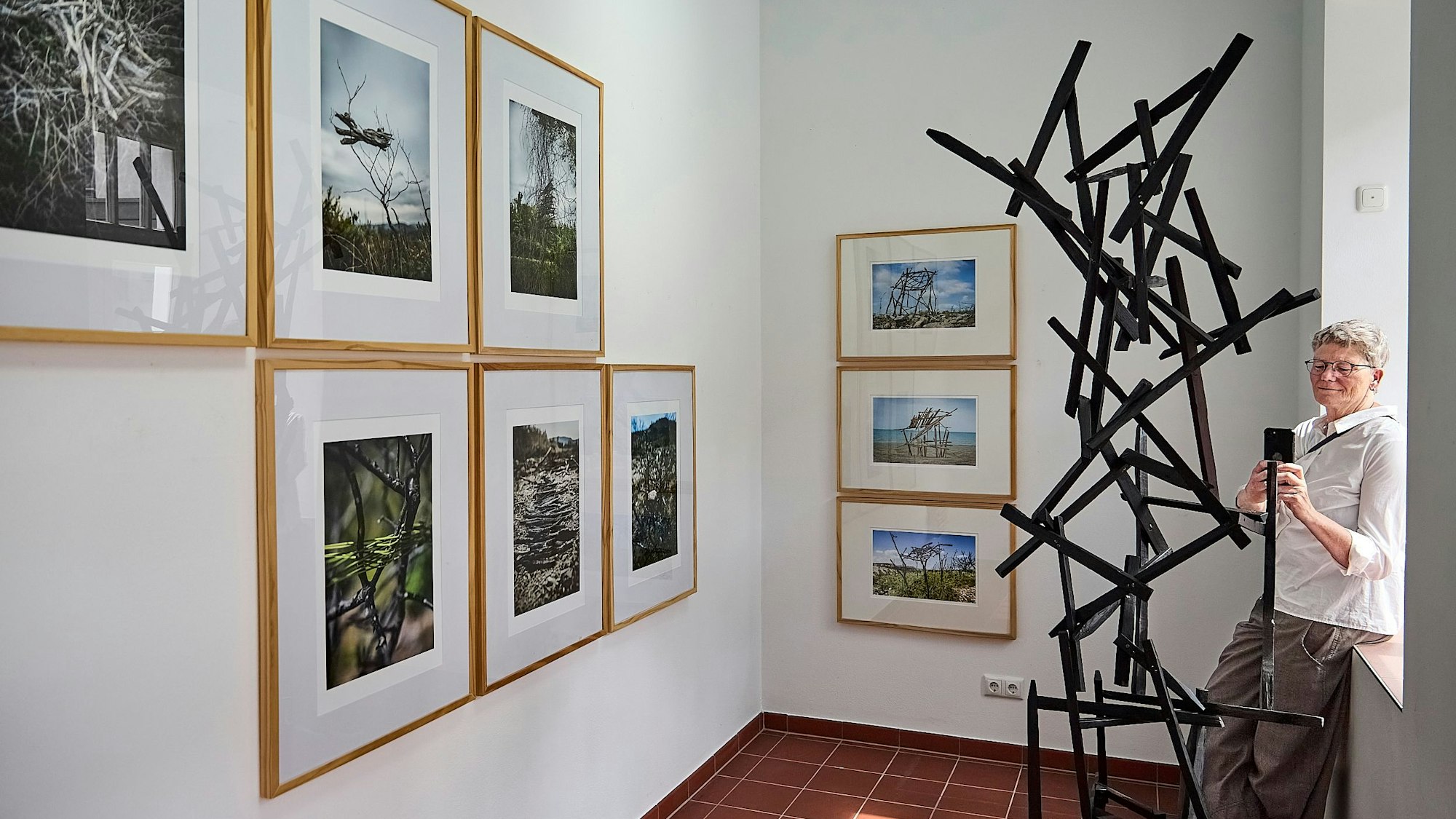 Rendel Freude lehnt an eine Fenstereinlassung und fotografiert eine Installation, die aus Stäben besteht.