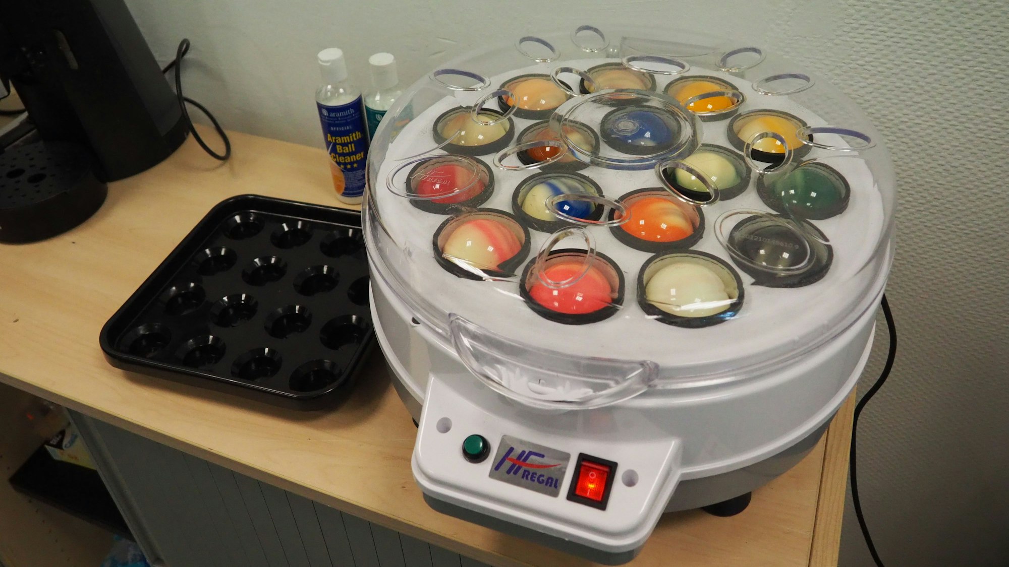 In der runden Poliermaschine sind unter dem Klarsichtdeckel einige bunte Billardkugeln zu sehen.