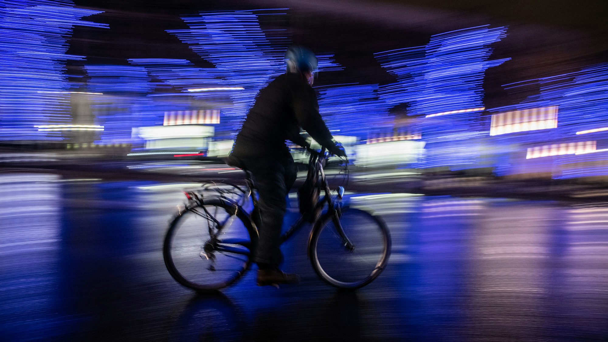 Ein Radfahrer fährt am Abend an illuminierten Bäumen auf der Straße.
