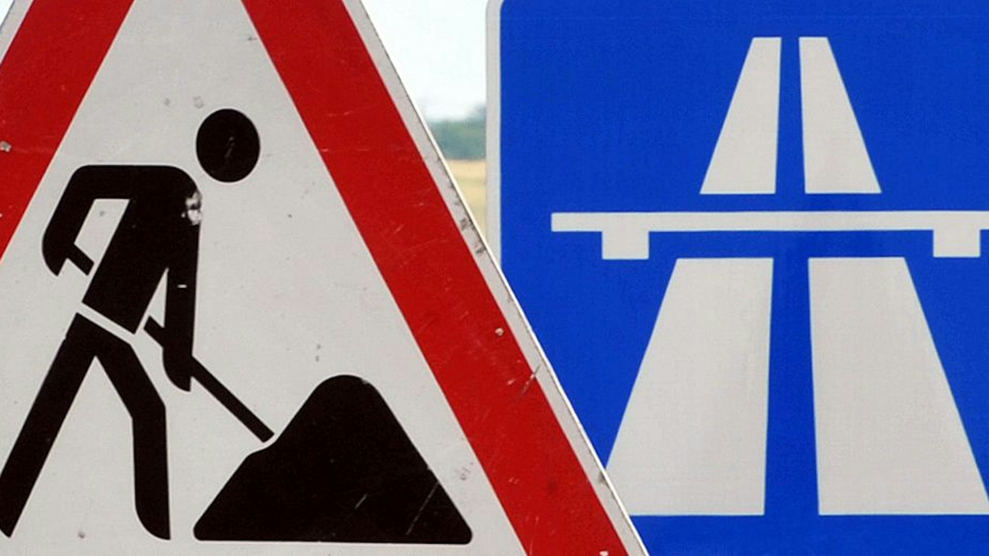 Ein Baustellenschild ist vor einem Autobahnschild platziert.