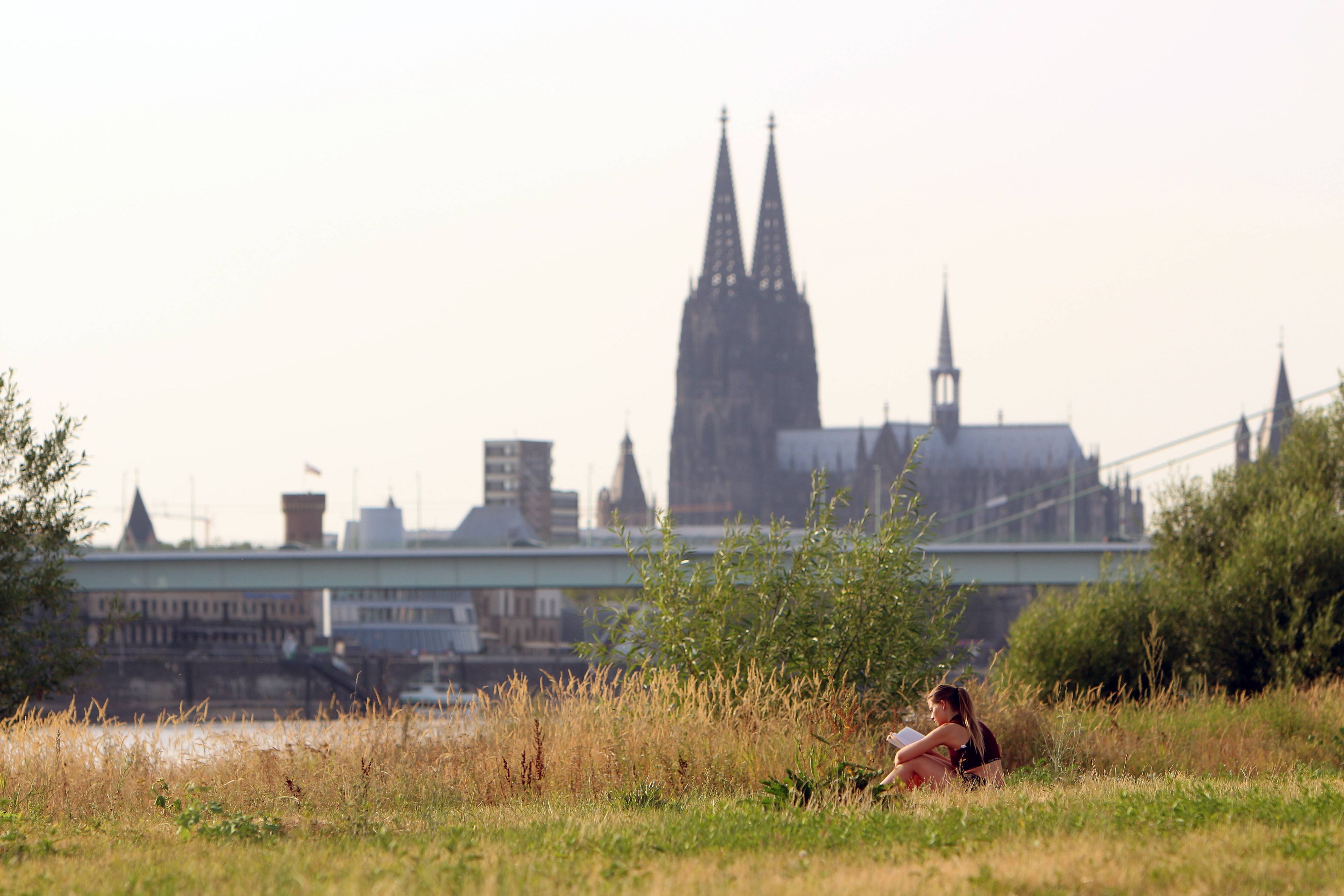 Sommerhitze in Köln am Rhein. Eine Frau entspannt sich mit einem Buch am Rheinufer in den Poller Auen vor dem Kölner Dom. (Archivfoto von 2025)