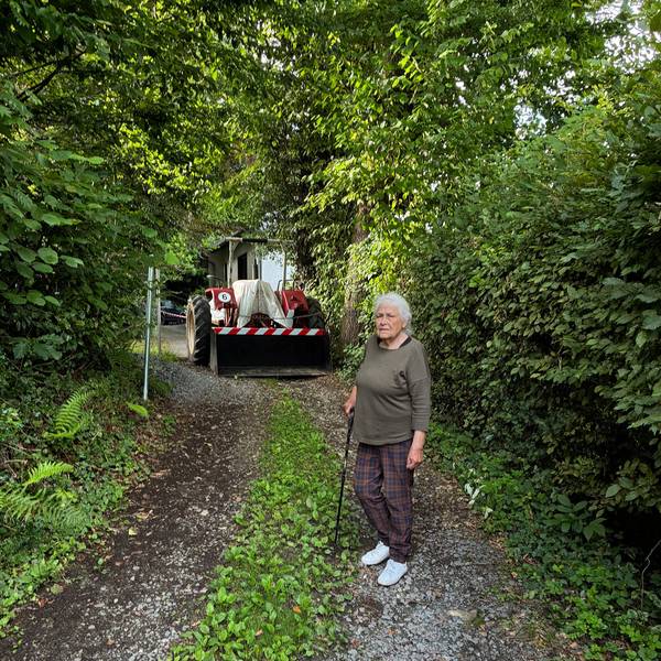 Irmintraut Fuchs steht, gestützt auf einen Stock, vor der Eisenkette und dem Trecker, die ihr den Weg zu ihrem Grundstück versperren.