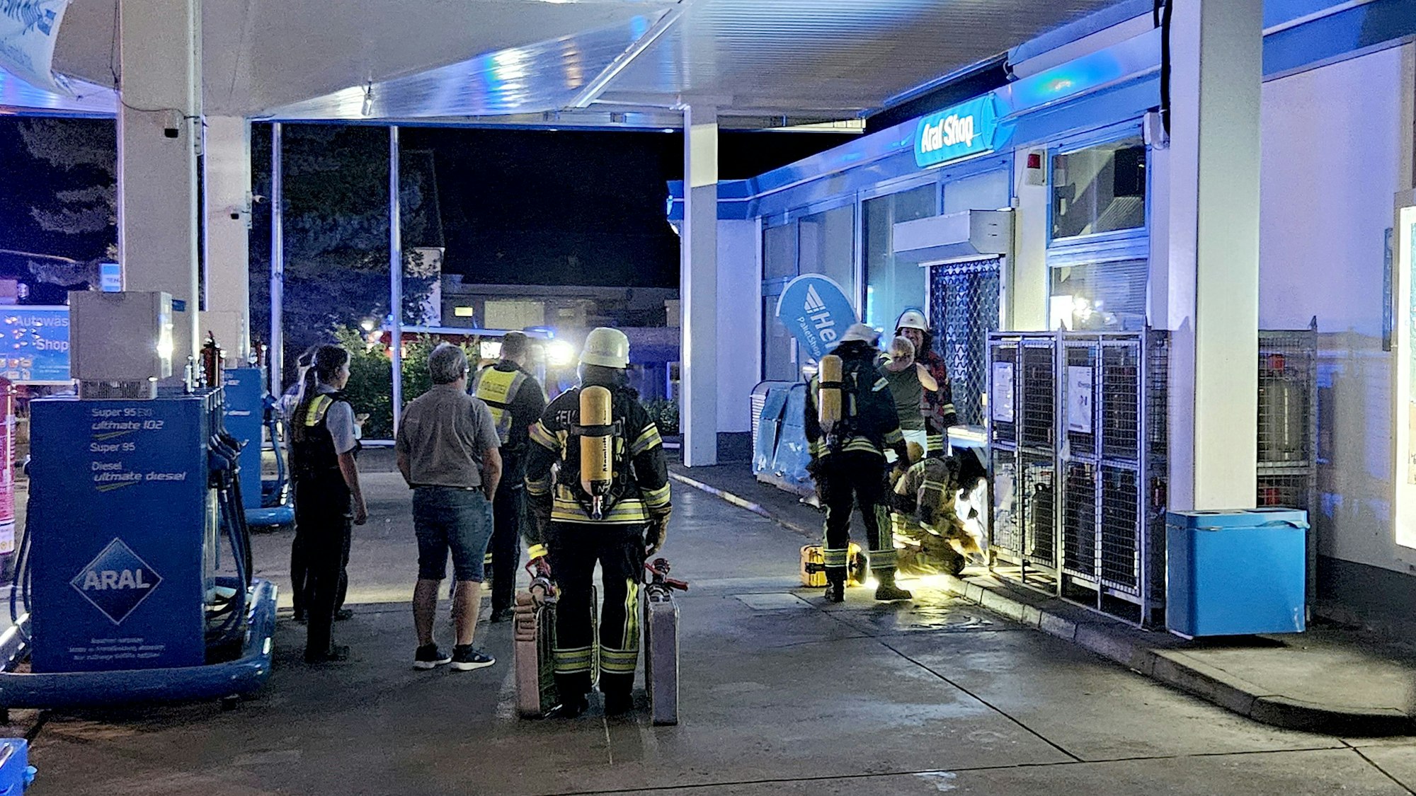 Feuerwehrleute und Polizei stehen vor der Tankstelle.