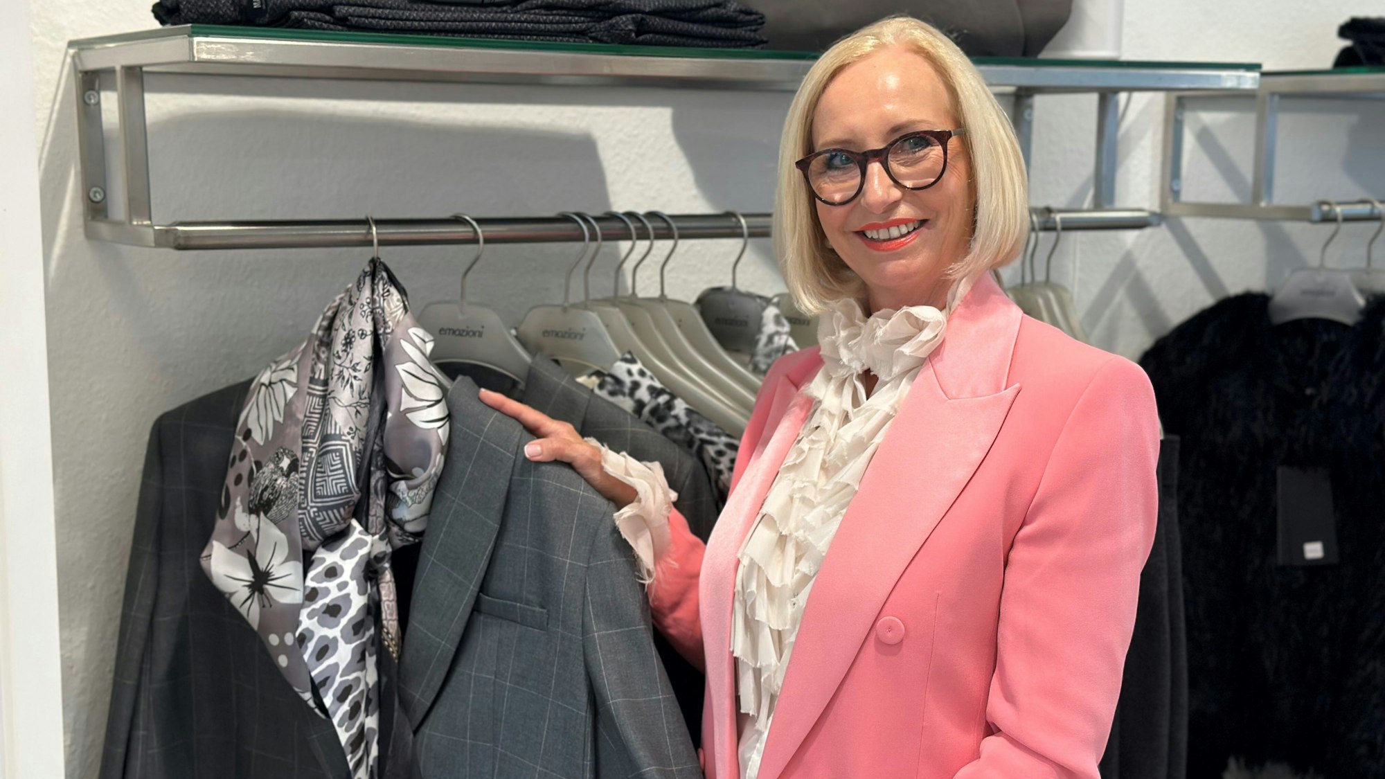 Eine Frau mit pinkem Blazer präsentiert einen grauen Blazer mit Tuch.