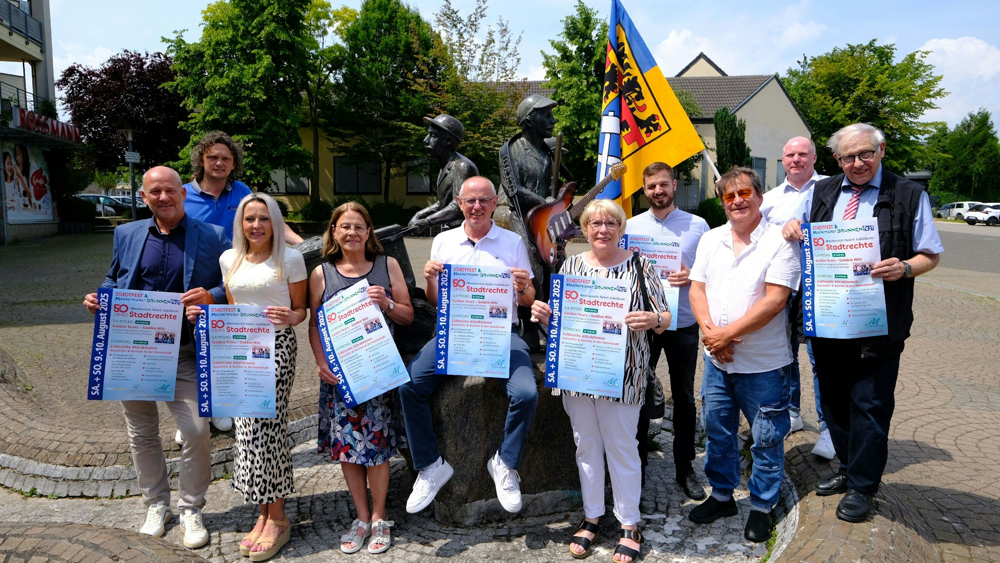 Programmvorstellung Brunnenfest: Das Orga-Team posiert mit Fahne und Plakaten am Mechernicher Marktplatz.