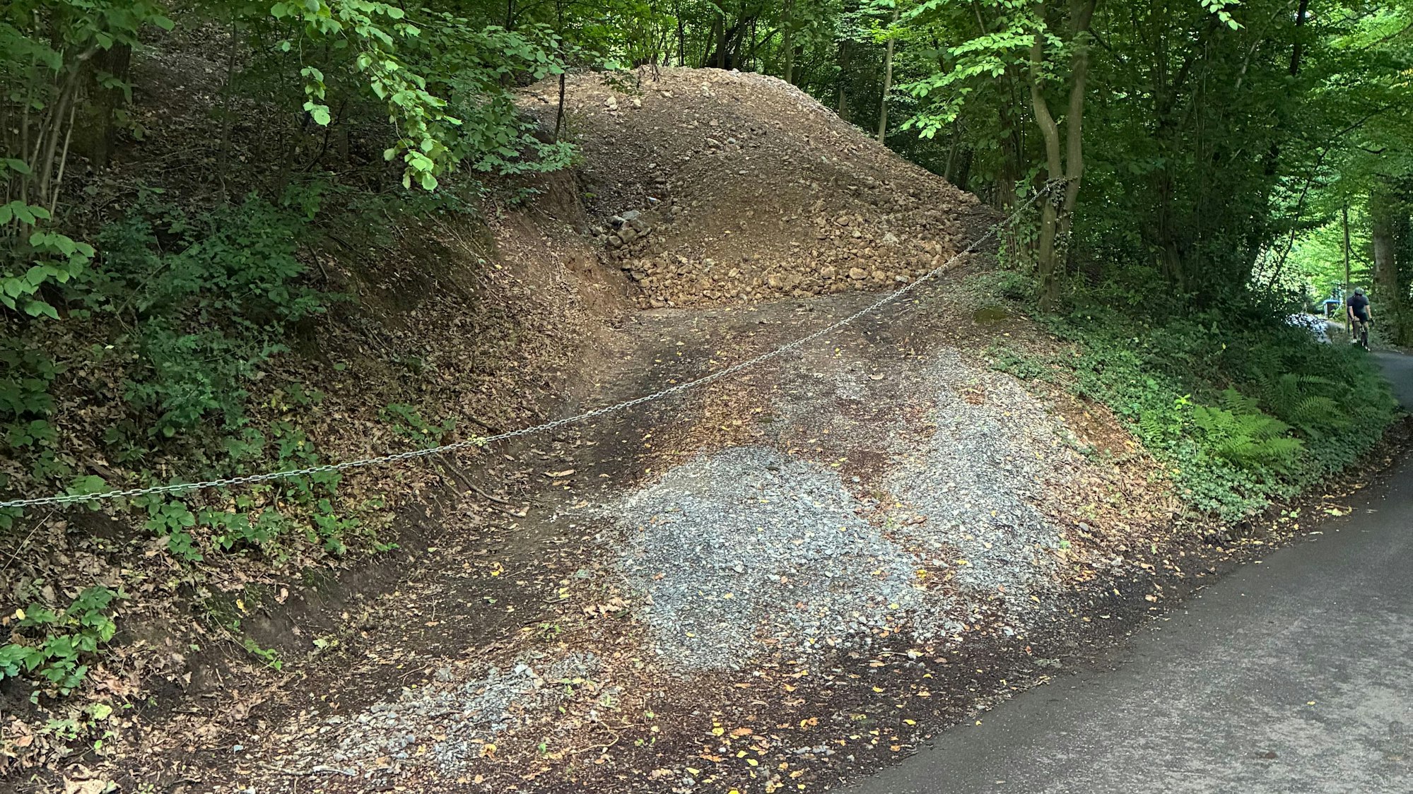 Ein Weg mit Erde und Schotter wird durch eine Kette versperrt.