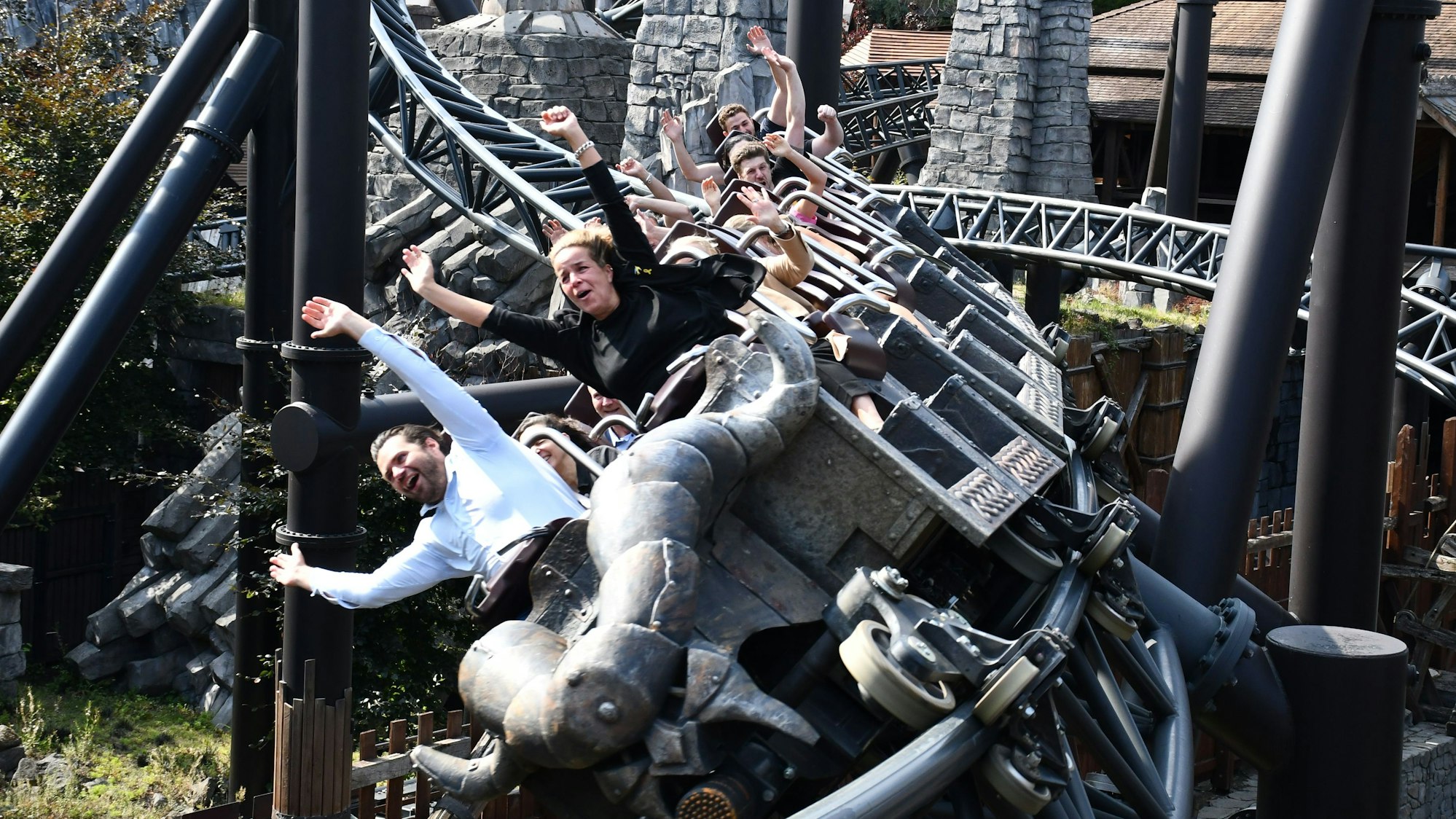 Das Foto zeigt die Ministerin mit hochgerissenen Armen vorn in einem voll besetzten Zug der Achterbahn, der sich gerade in die Kurve legt.