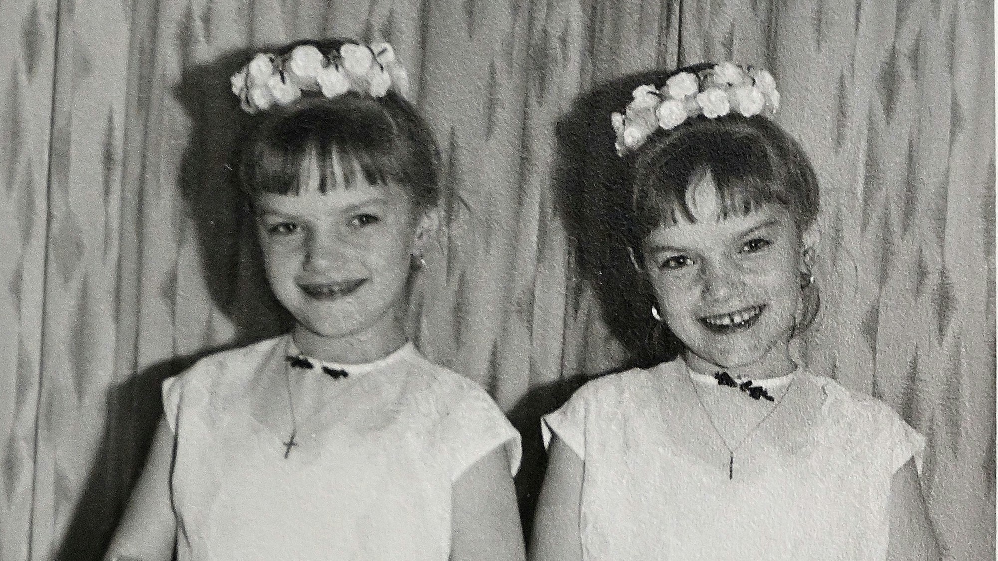 Auf einem Kinderfoto tragen die Zwillinge jeweils einen Blumenkranz und ein weißes Kleid.