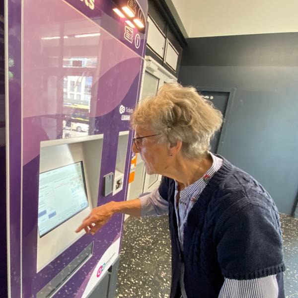 Eine ältere Dame steht an einem Ticketautomaten und schaut konzentriert auf das Display.