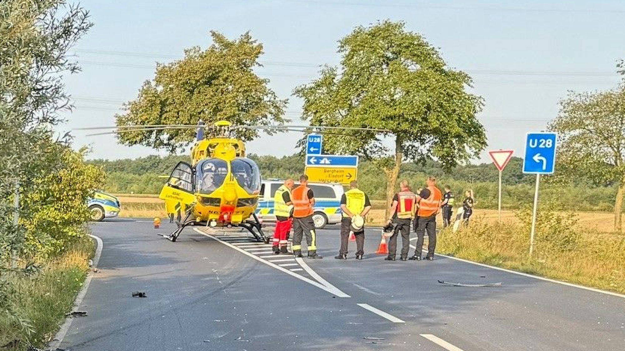 Das Bild zeigt eine Straßeneinmündung mit Einsatzkräften der Feuerwehr und einem Rettungshubschrauber