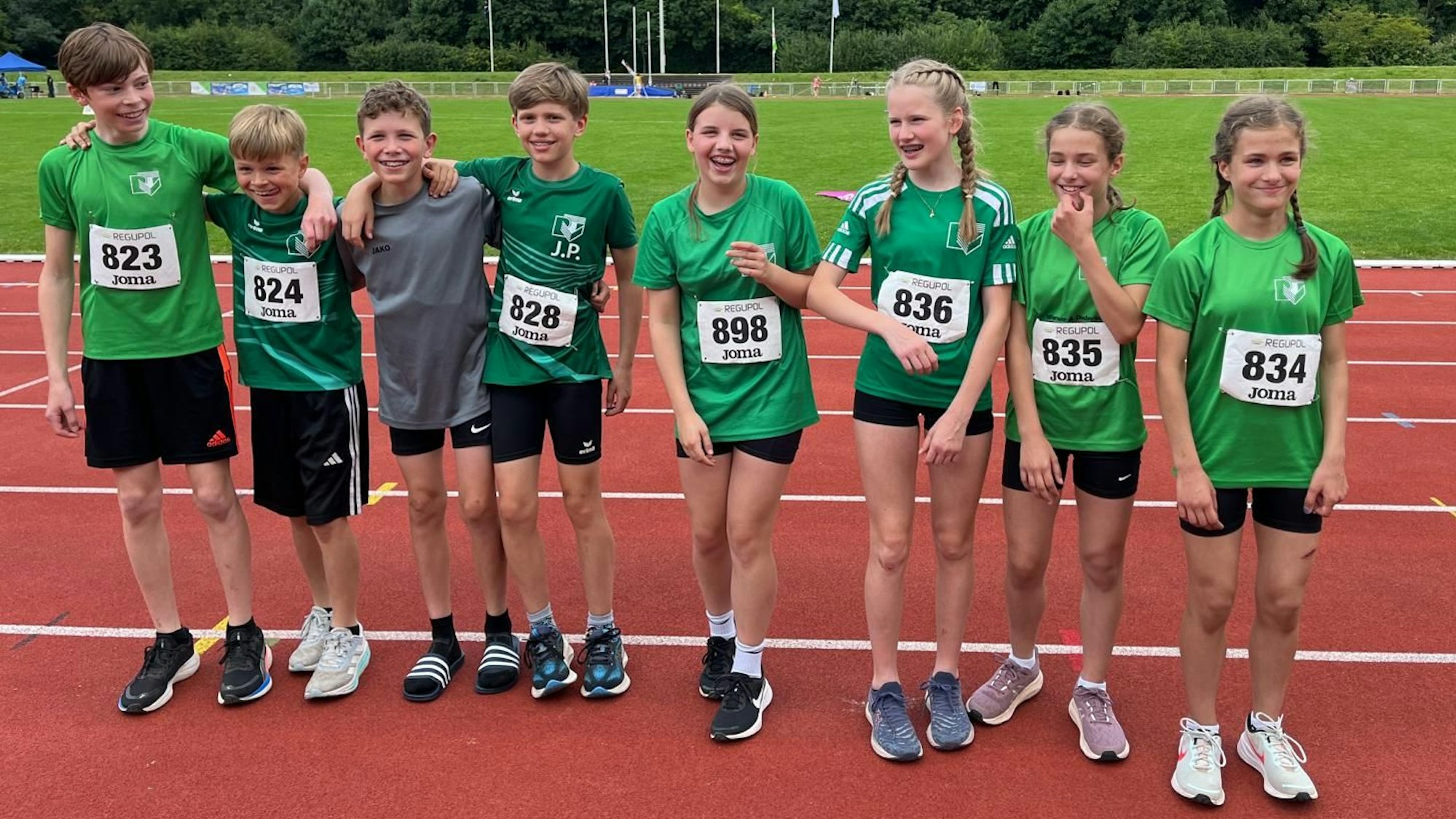 Die vier Jungs und vier Mädchen in Laufshirts stehen nebeneinander auf einer Tartanbahn.