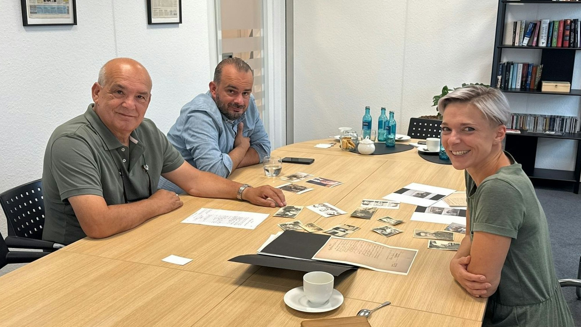Drei Menschen an einem Tisch, auf dem Fotos liegen.