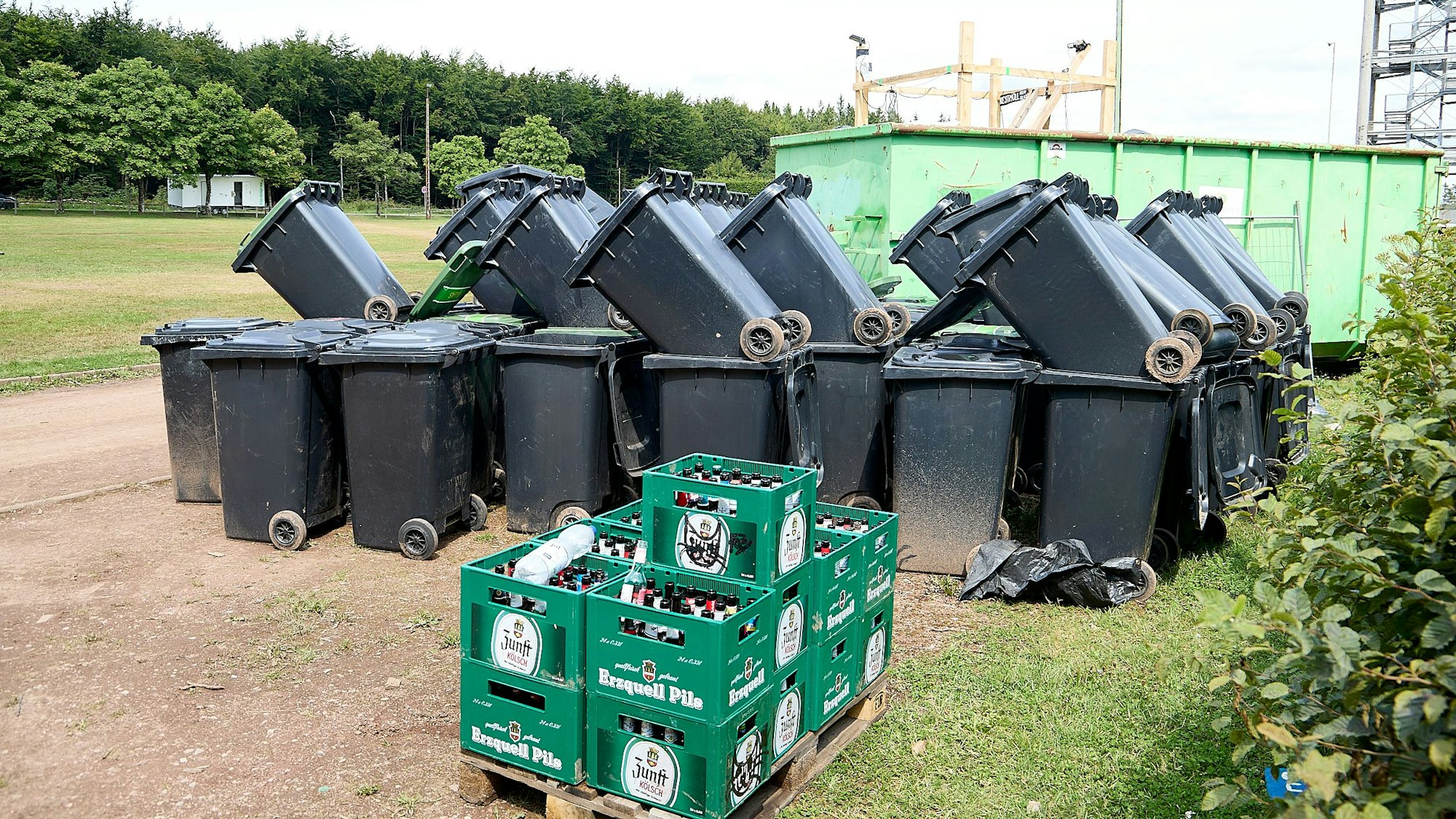 Zahlreiche Restmülltonnen sind aufeinander gestapelt, davor Kästen mit Pfandflaschen.
