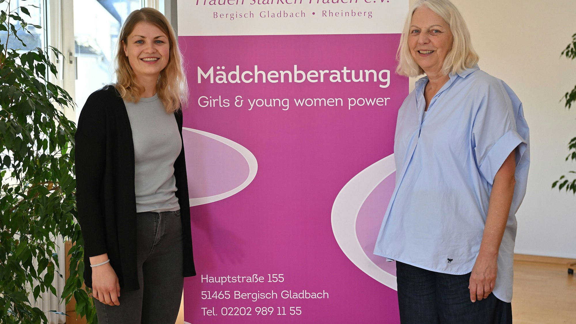 Die beiden Frauen stehen nebeneinander vor einem Plakat.