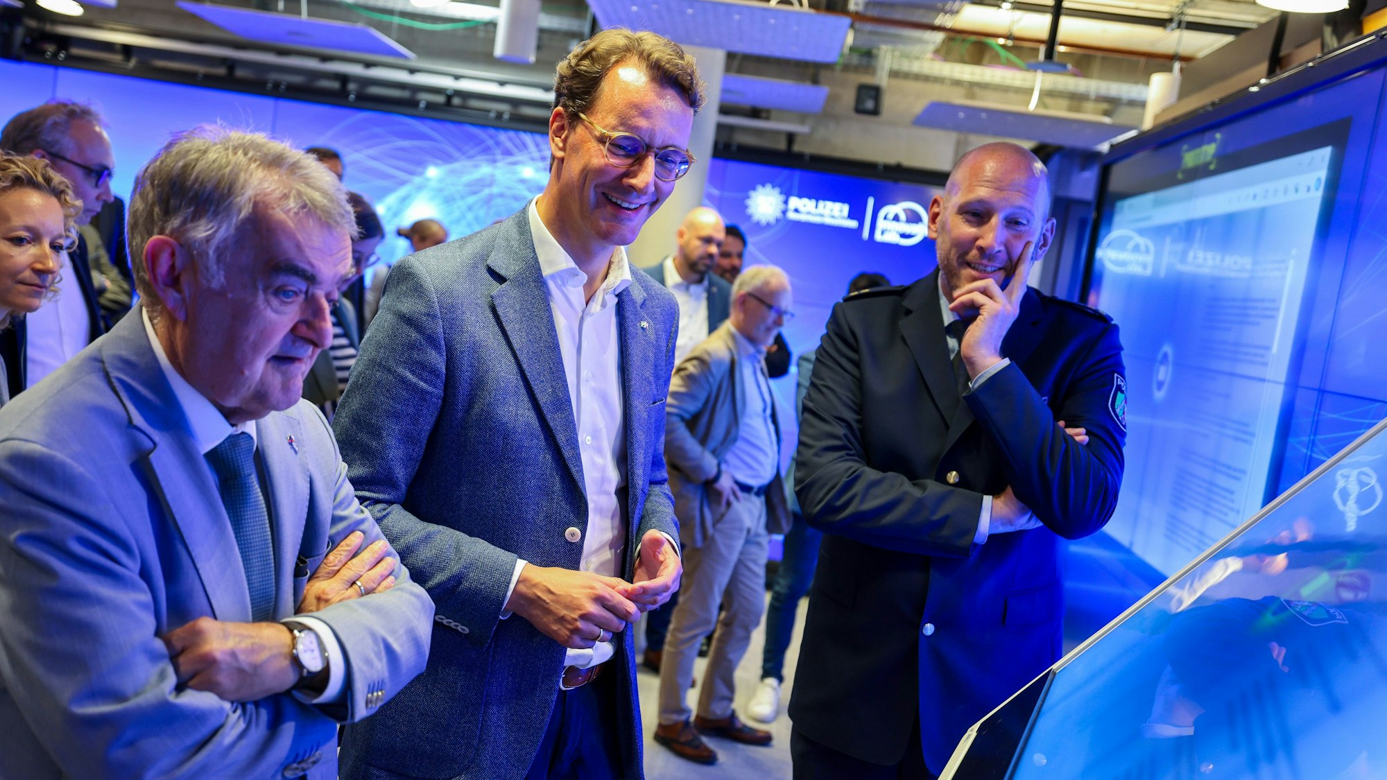 Im „Innovation Lab“ der Polizei NRW benutzen Innenminister Herbert Reul, Ministerpräsident Hendrik Wüst und Dominic Reese, Leiter des Innovation Lab, einen Monitor mit Anwendungen künstlicher Intelligenz. (Archivfoto)