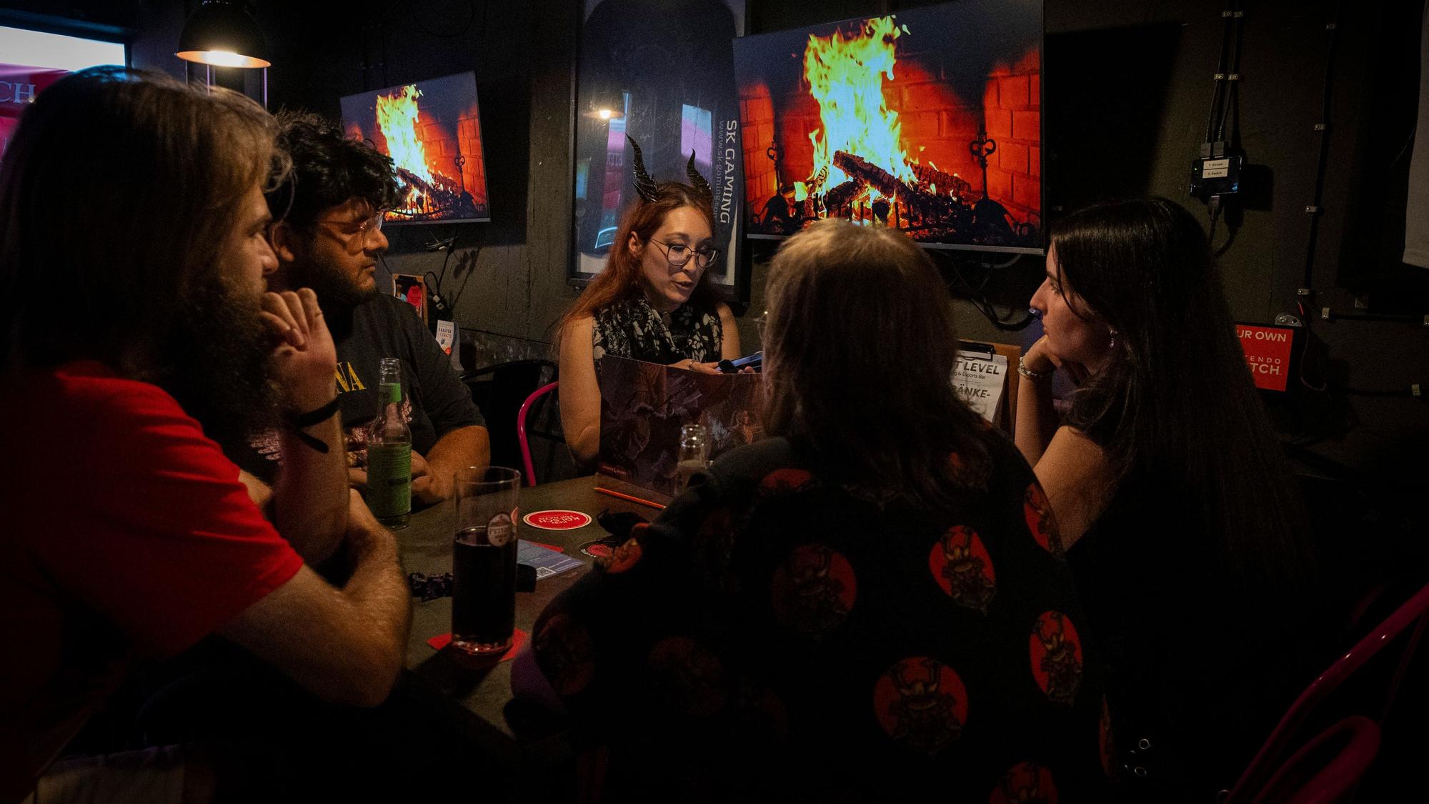 Fünf Personen sitzen an einem Tisch und spielen das Rollenspiel „Pen and Paper.“