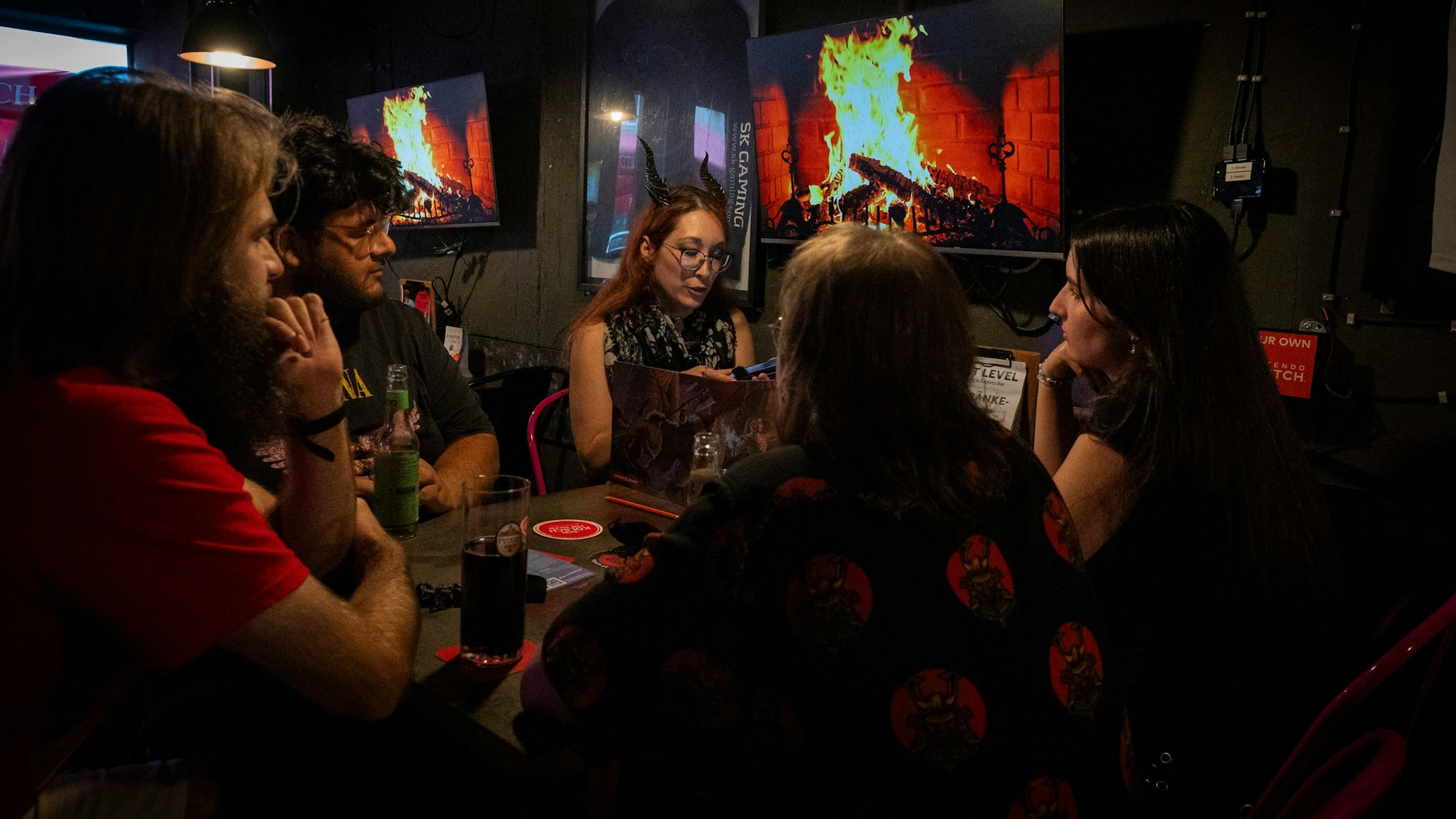 Fünf Personen sitzen an einem Tisch und spielen das Rollenspiel „Pen and Paper.“