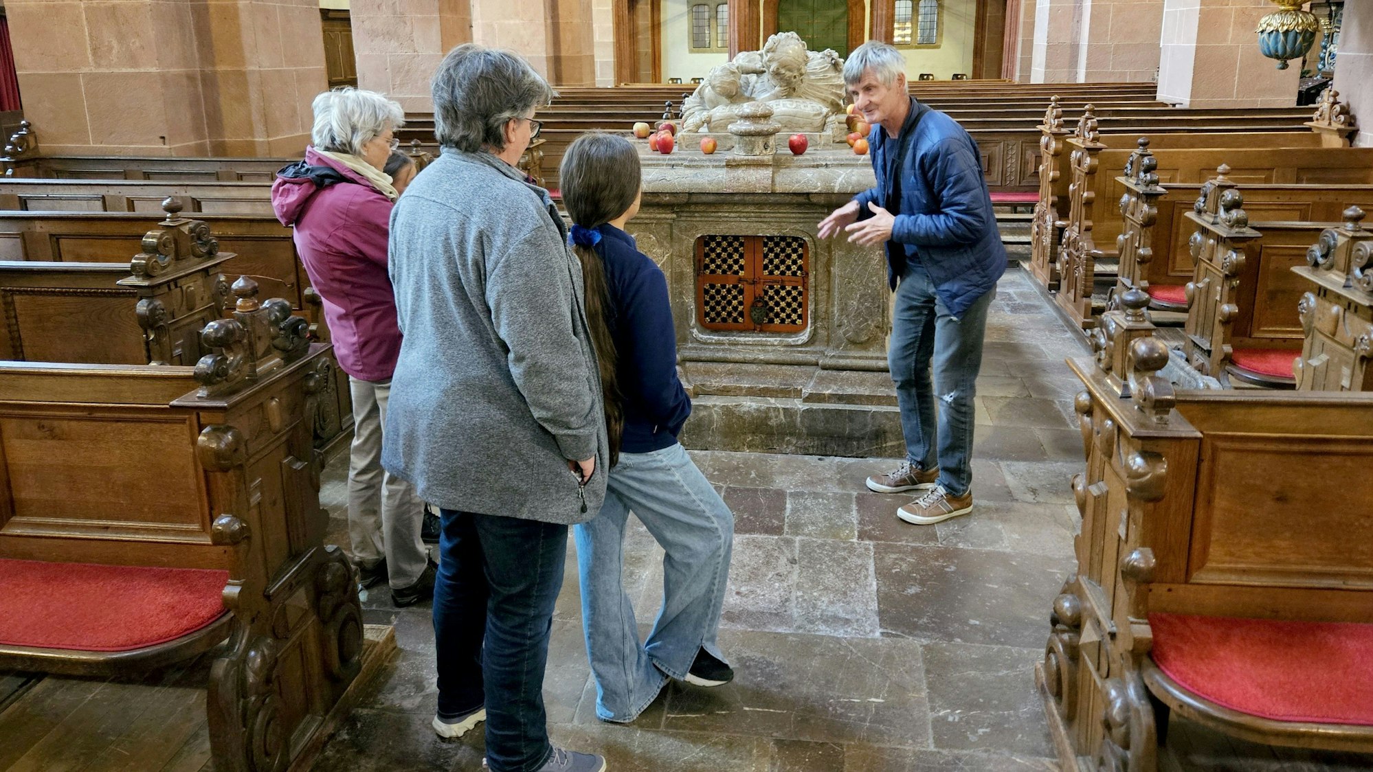 Stefan Hönig gestikuliert vor einem Sarkophag in der Steinfelder Basilika. Kinder und ältere Frauen schauen ihn an.