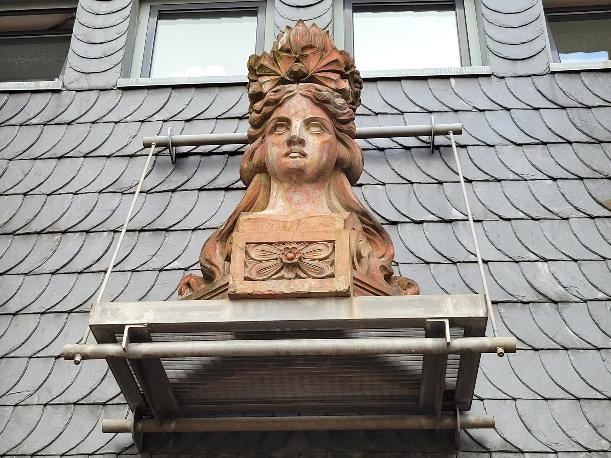 Eine Büste, sie zeigt eine Frau, sie hängt an einer Fassade.