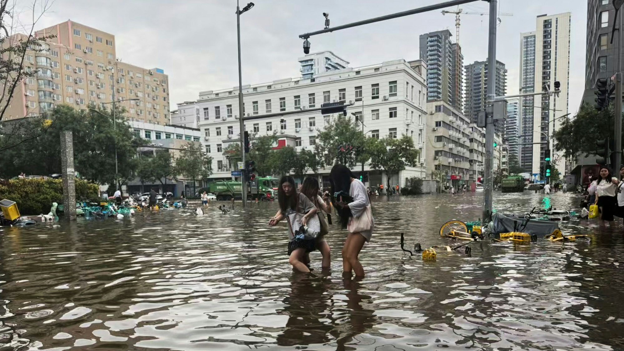 Frauen waten nach starken Regenfällen durch eine überschwemmte Straße in der zentralchinesischen Provinz Henan.