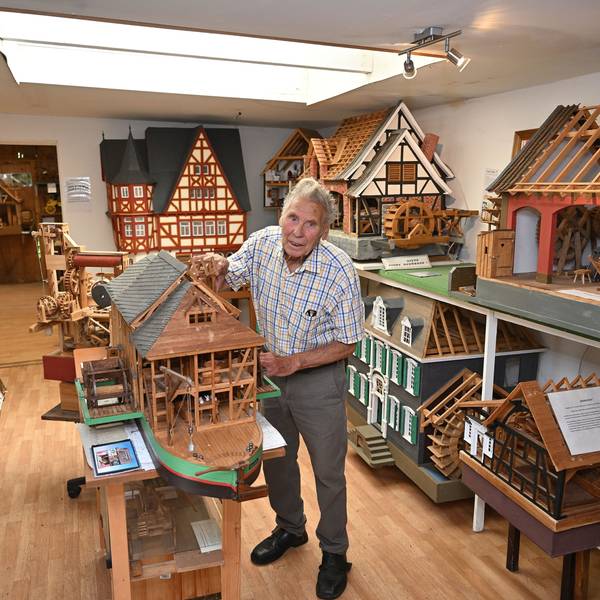 Ein alter Mann steht in einem Raum mit zahlreichen Holzmodellen von Häusern und Mühlen