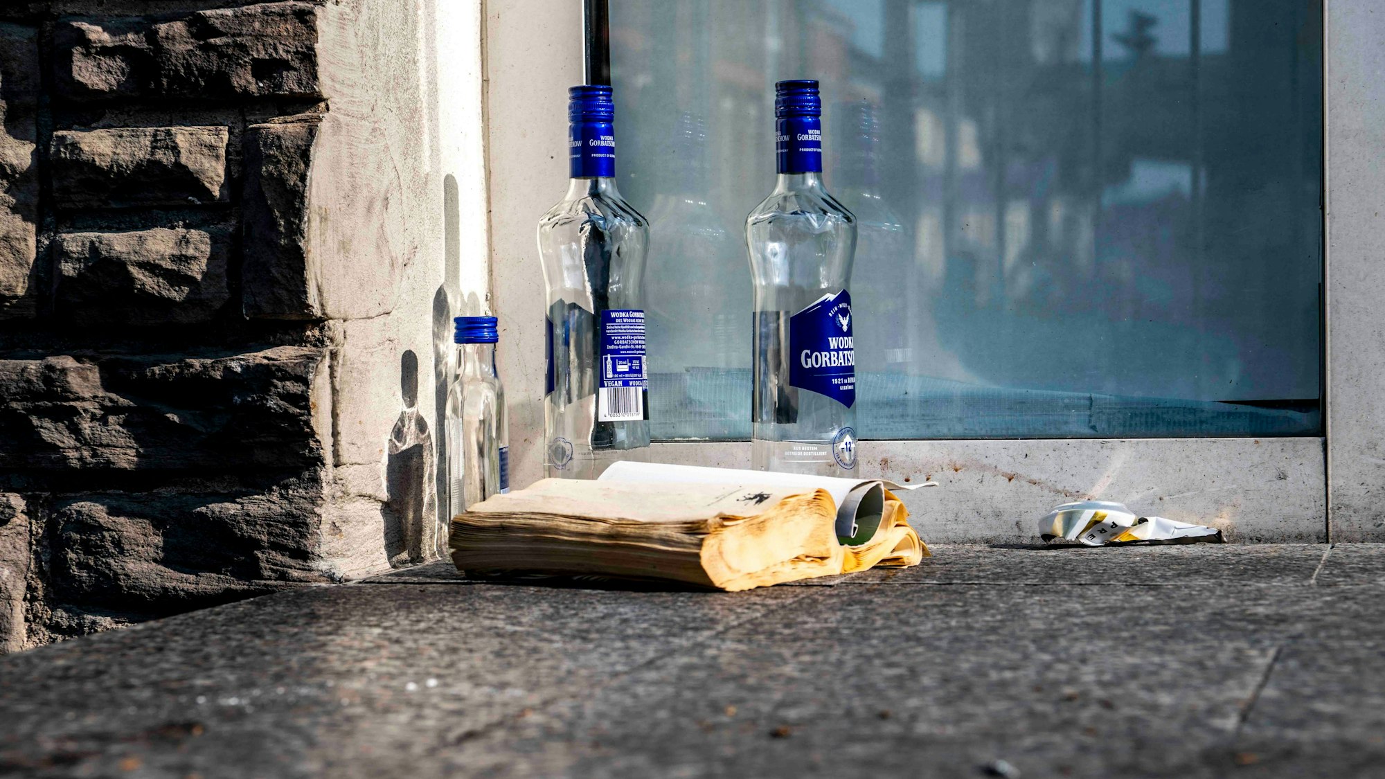 Das Bild zeigt drei leere Flaschen Alkohol und ein Buch auf einer Treppe am Euskirchener Bahnhof.