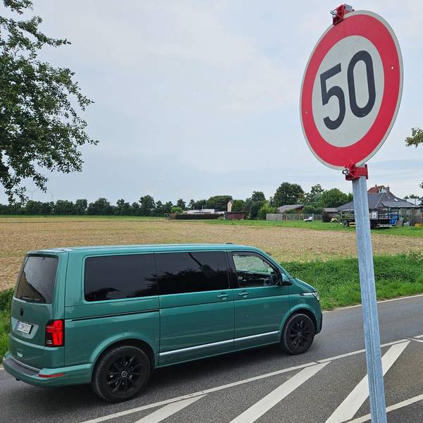 Zu sehen ist eine Straße und daneben ein Metallrahmen, in dem ein Ortseingangsschild fehlt, sowie ein provisorisch aufgestelltes Tempo-50-Schild.