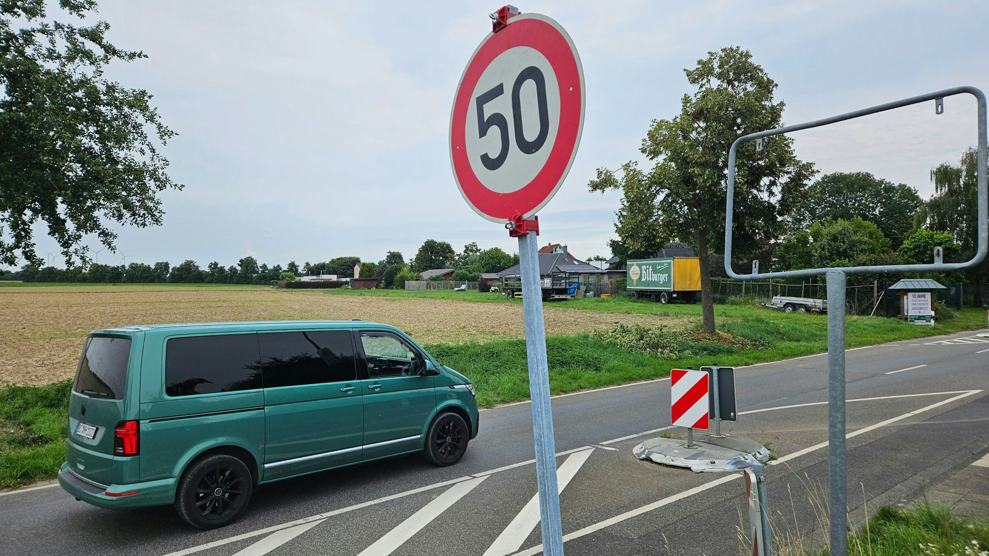 Zu sehen ist eine Straße und daneben ein Metallrahmen, in dem ein Ortseingangsschild fehlt, sowie ein provisorisch aufgestelltes Tempo-50-Schild.
