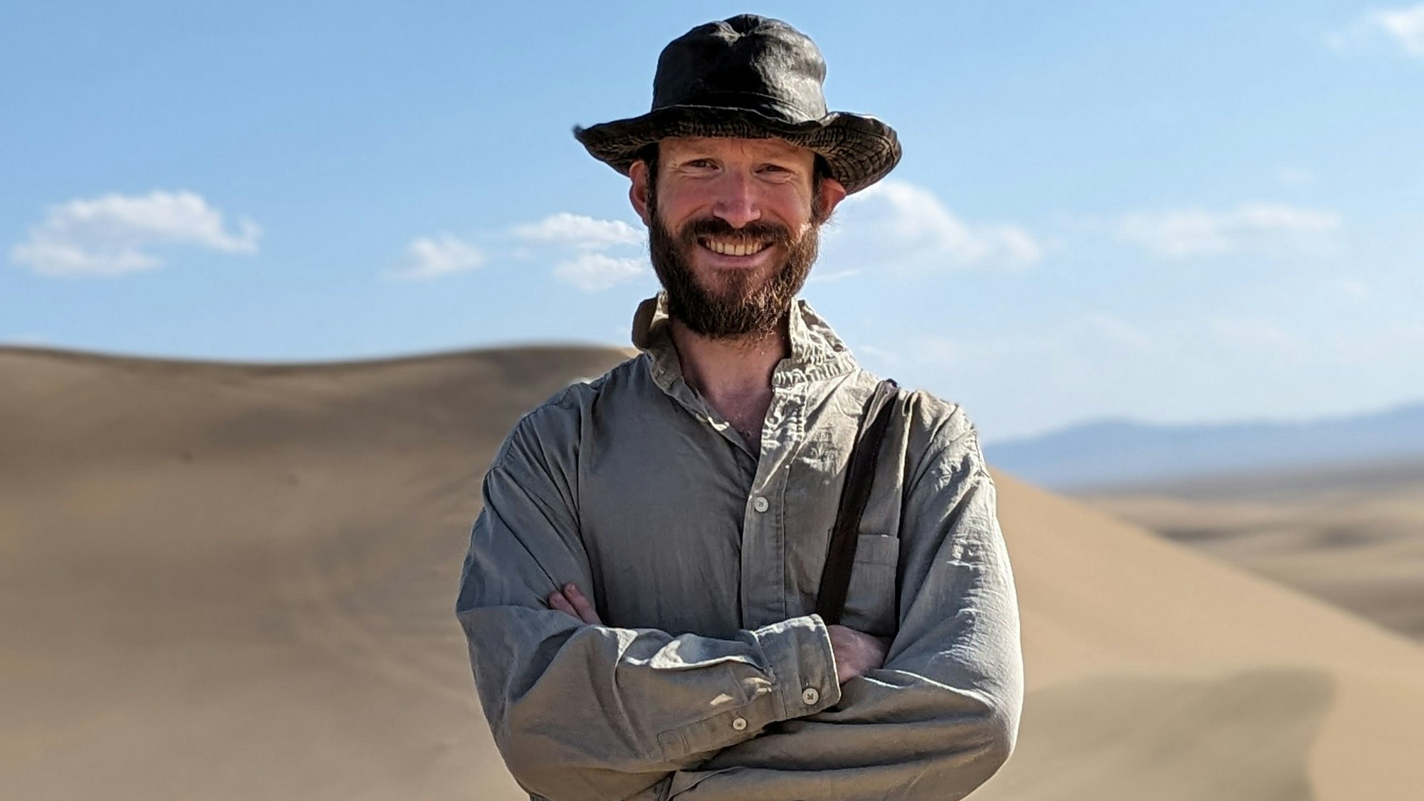 Ein Mann steht mit Hut in der Wüste.