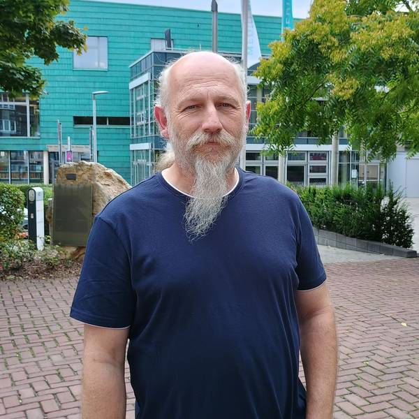 Peter Hirseler trägt ein dunkelblaues T-Shirt und hat einen Bart. Hinter ihm sieht man einige Bäume und das Medio Rhein Erft.