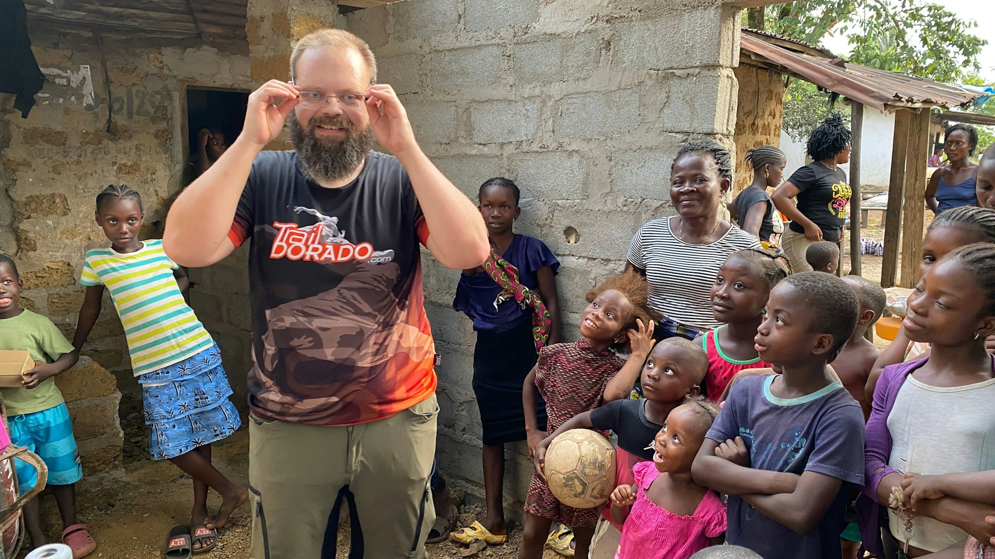 Ein Mann mit Brille steht in Mitte vieler Kinder in einem Dorf in Liberia.