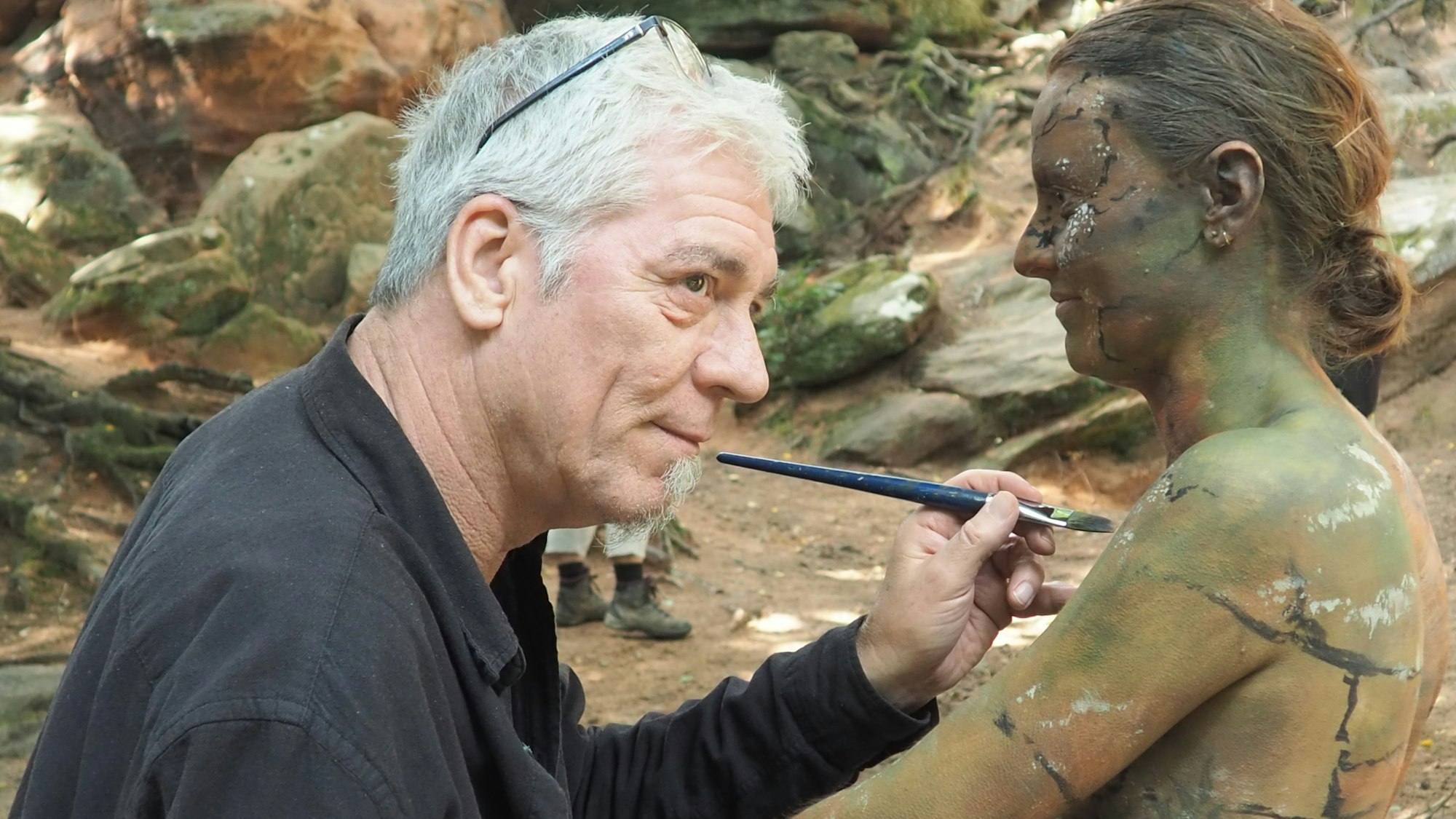 Jörg Düsterwald tupft mit dem Pinsel neue Farbe auf Carolina Müller-Neuhaus' Haut.