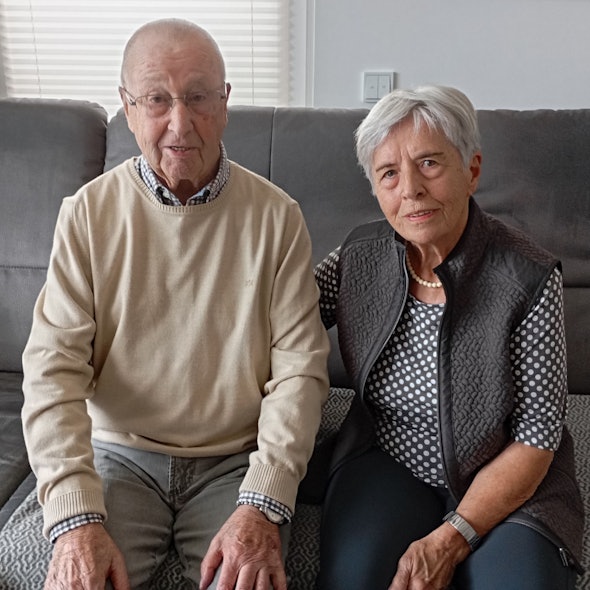 Die beiden sitzen auf einem Sofa. Ingeborg Schulte legt den Arm auf den Rücken ihres Mannes .