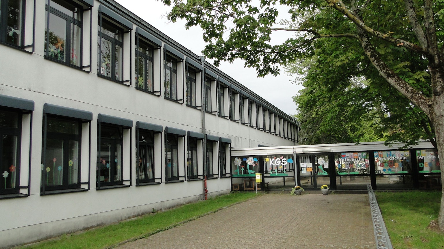 Ein langgezogenes, zweigeschossiges Gebäude ist durch einen verglasten Eingang zu betreten.