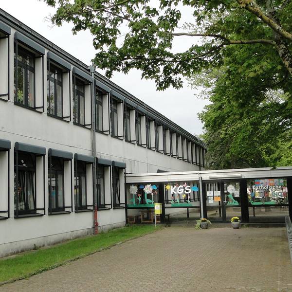 Ein langgezogenes, zweigeschossiges Gebäude ist durch einen verglasten Eingang zu betreten.