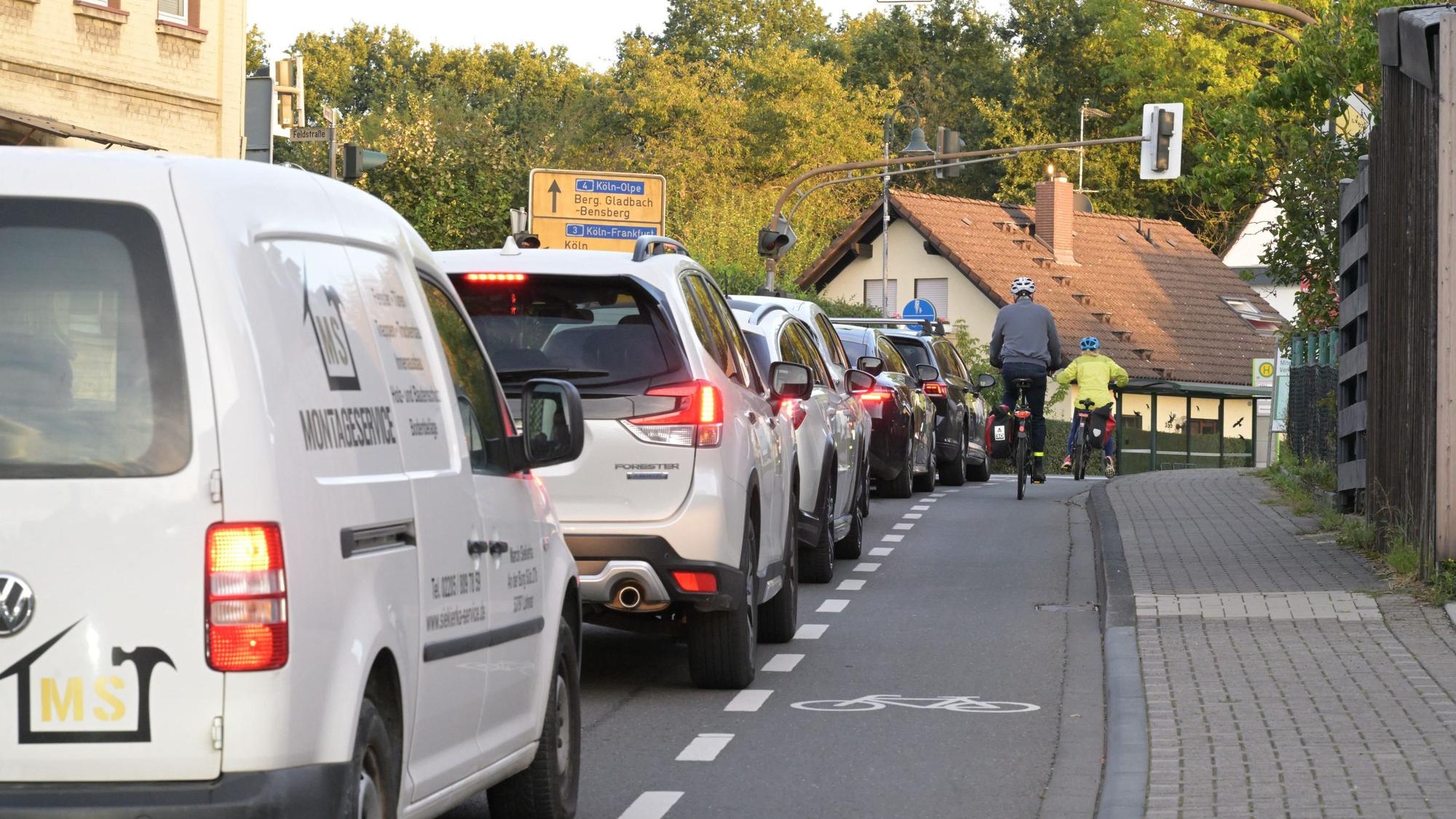 Zwei Radfahrer fahren über einen Radstreifen auf der Fahrbahn. Neben ihnen viele Autos.