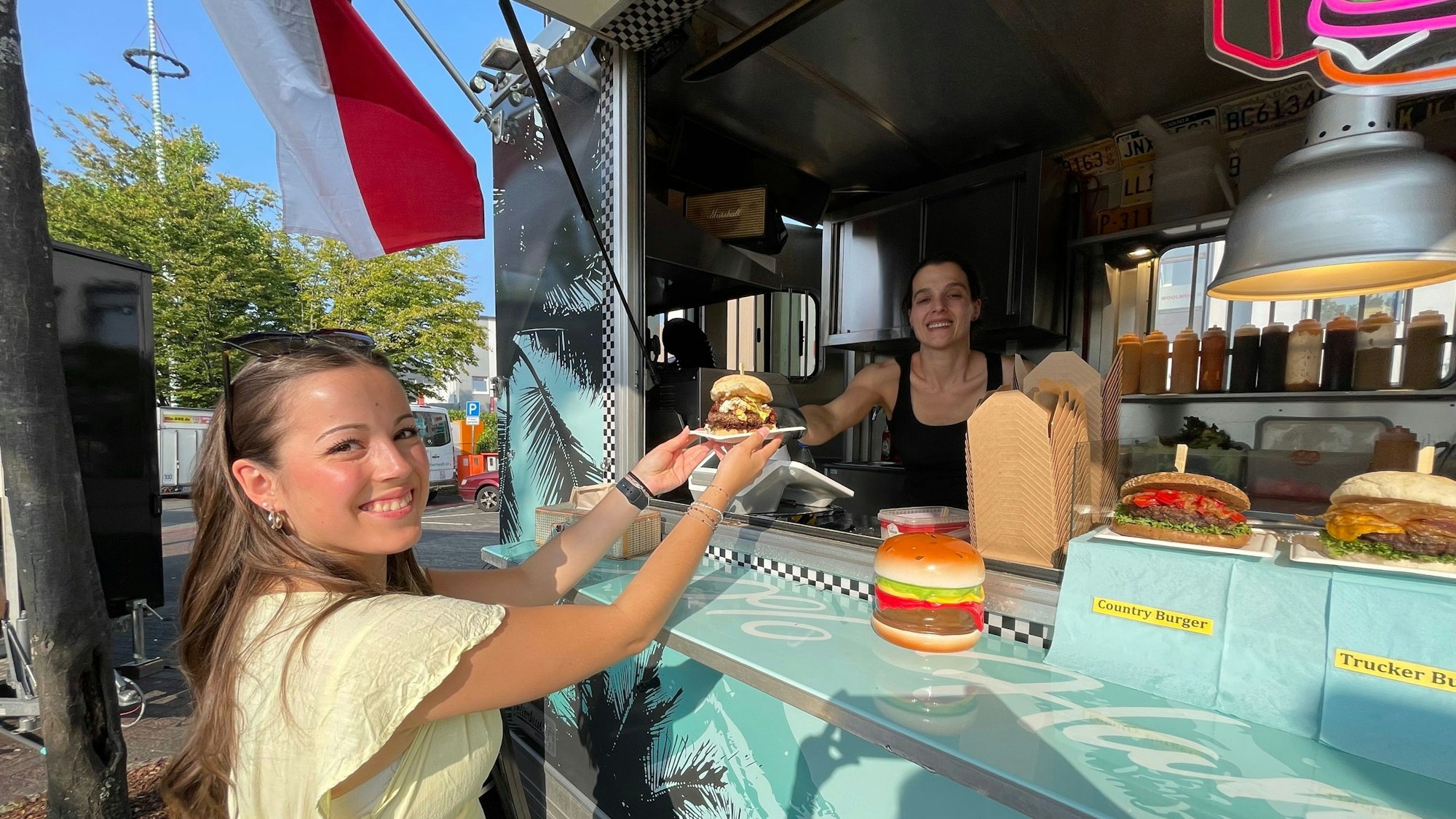 Eine junge Frau nimmt glücklich ihren Burger von der Verkäuferin entgegen.