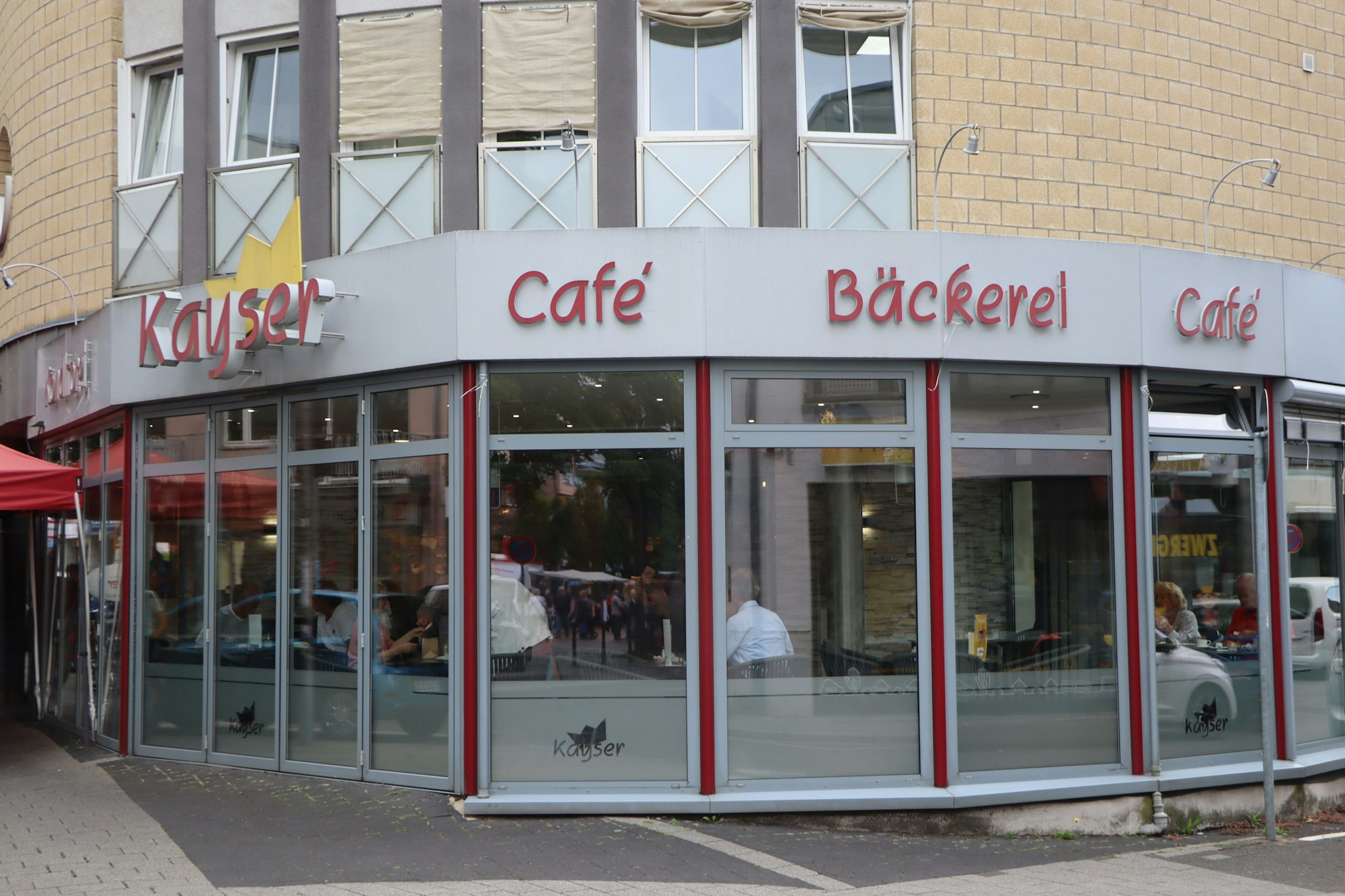 Zu sehen ist das großzügig verglaste Gebäude der Bäckerei. Als Logo hinter der Aufschrift Kayser fungiert eine Krone.