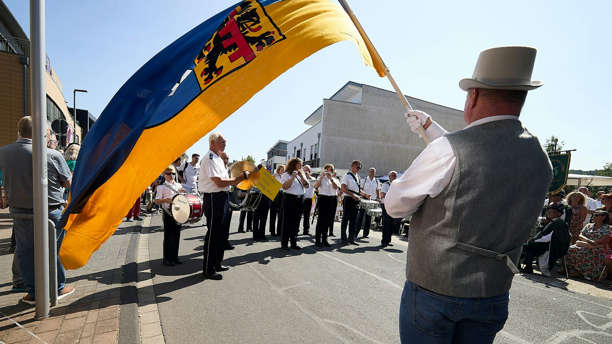 Blick unter einer großen Stadtfahne, die von einem Mann mit Zylinder gehalten wird, hindurch auf die Musikkapelle.