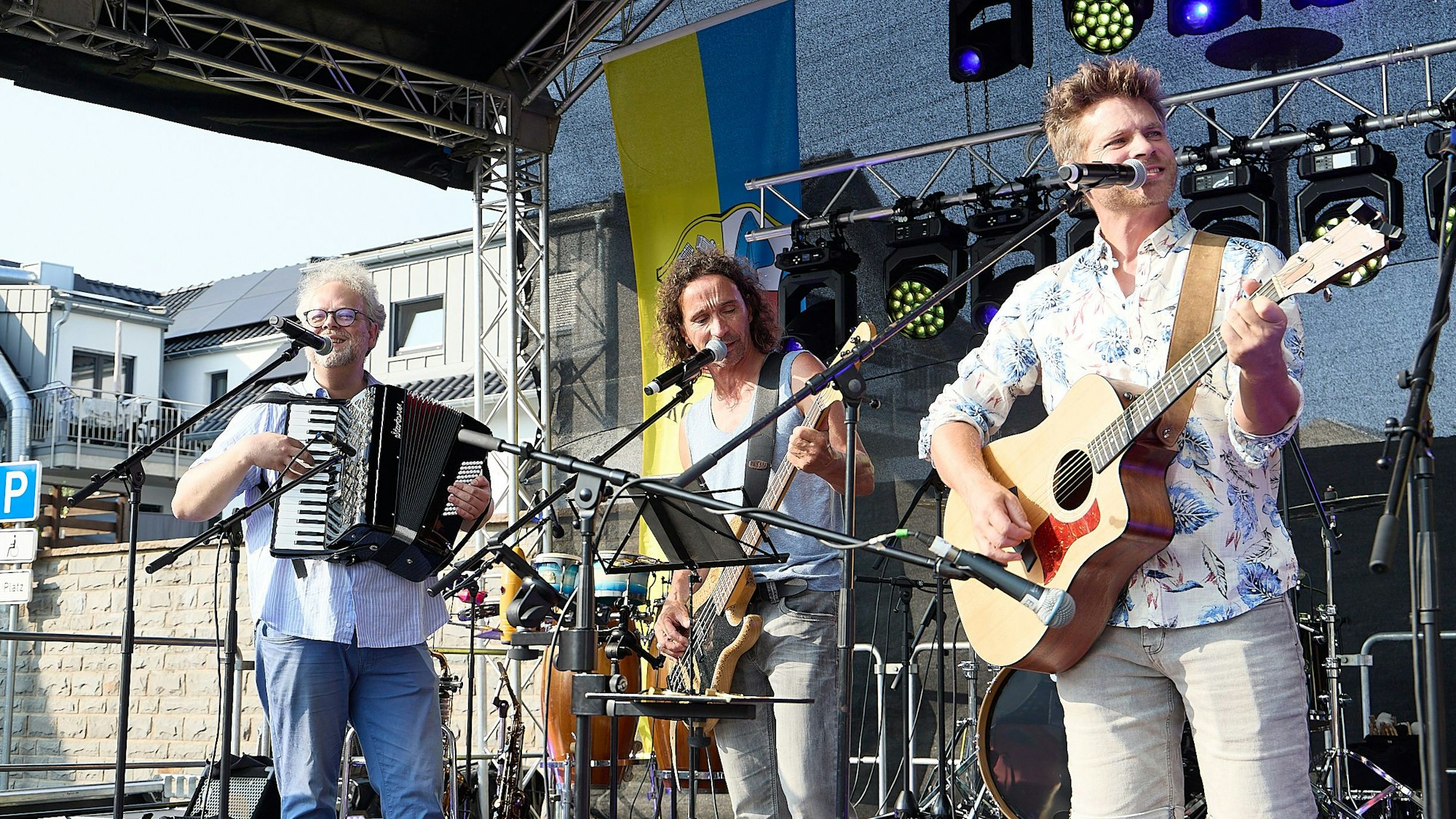 Erik Arndt mit Akkordeon, Stephan Brings mit Bass und Uwe Reetz mit Gitarre stehen nebeneinander auf der Bühne.