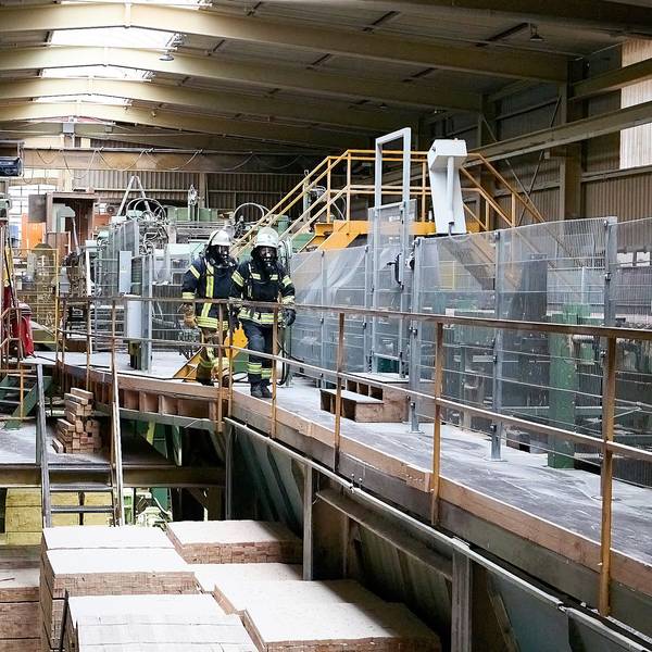 Zwei Feuerwehrmänner unter Atemschutz gehen durch eine der Produktionshallen.