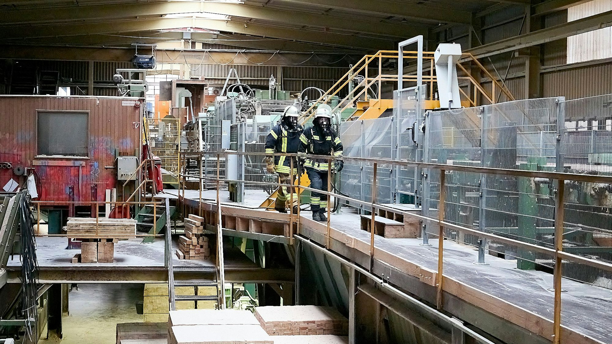 Zwei Feuerwehrmänner unter Atemschutz gehen durch eine der Produktionshallen.