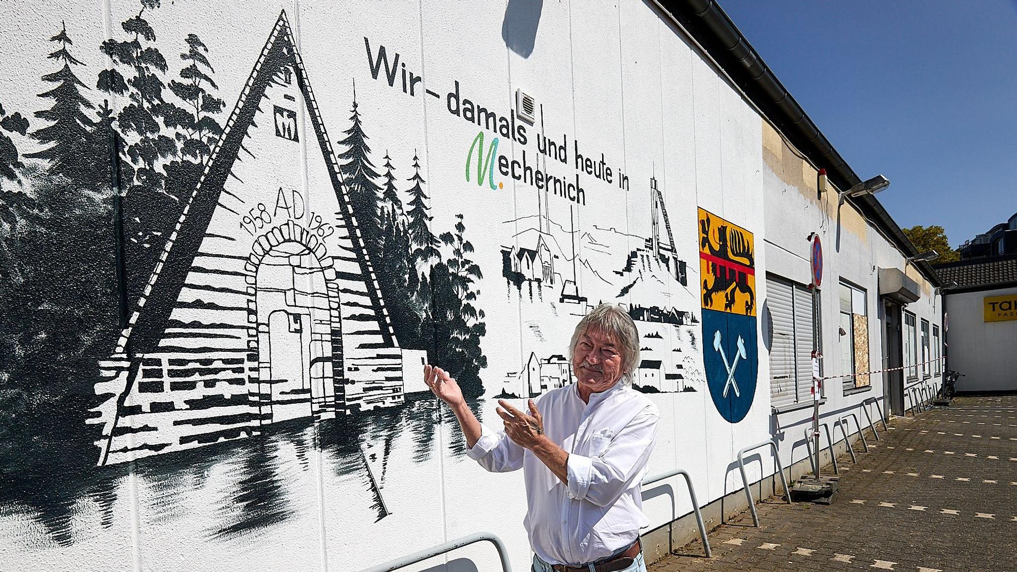 Yklas Kozikejew steht vor seinem Bild auf der Wand eines Gebäudes und zeigt darauf.